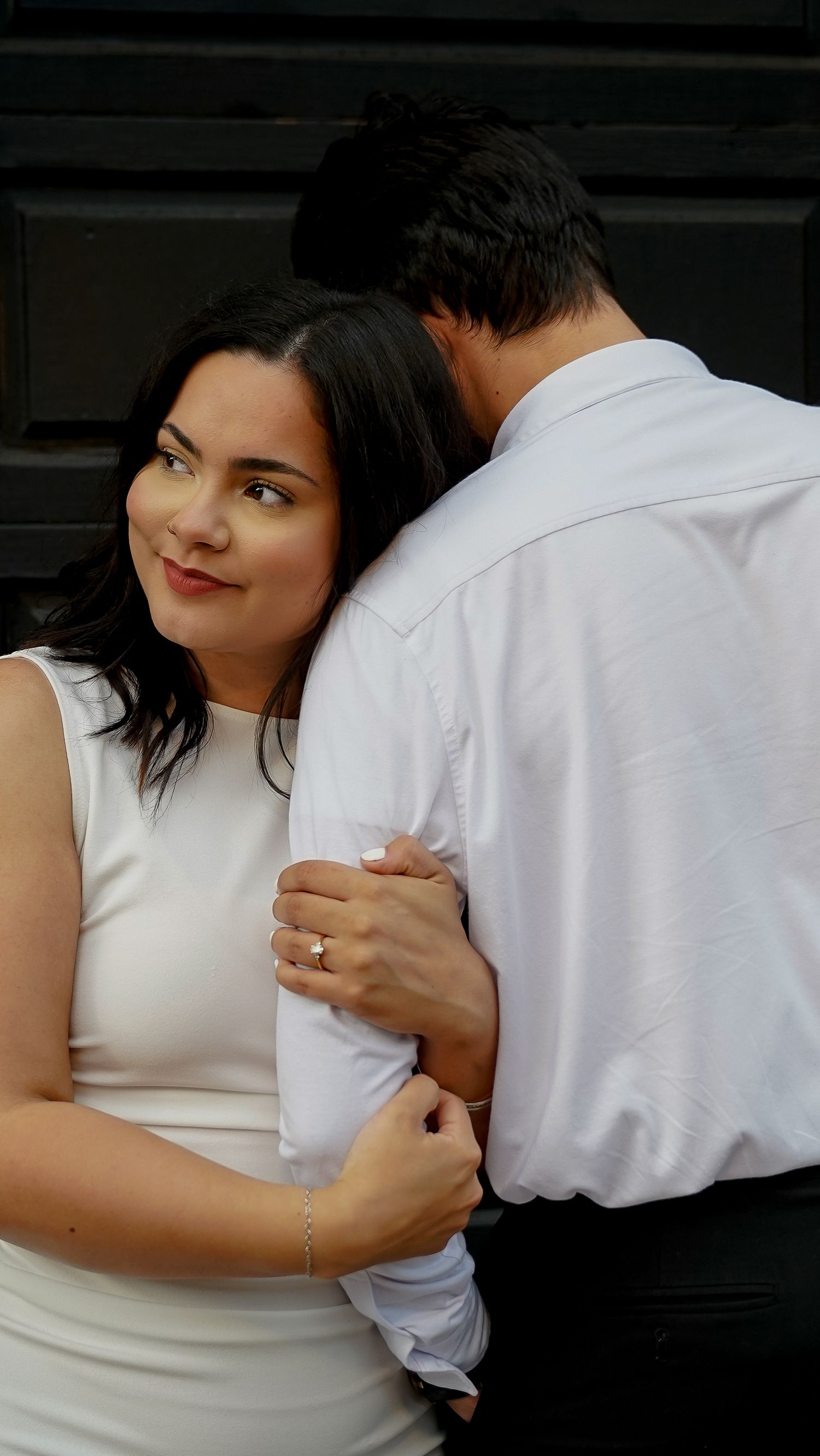 Romantic couple in white clothing embrace intimately while posing for a portrait.