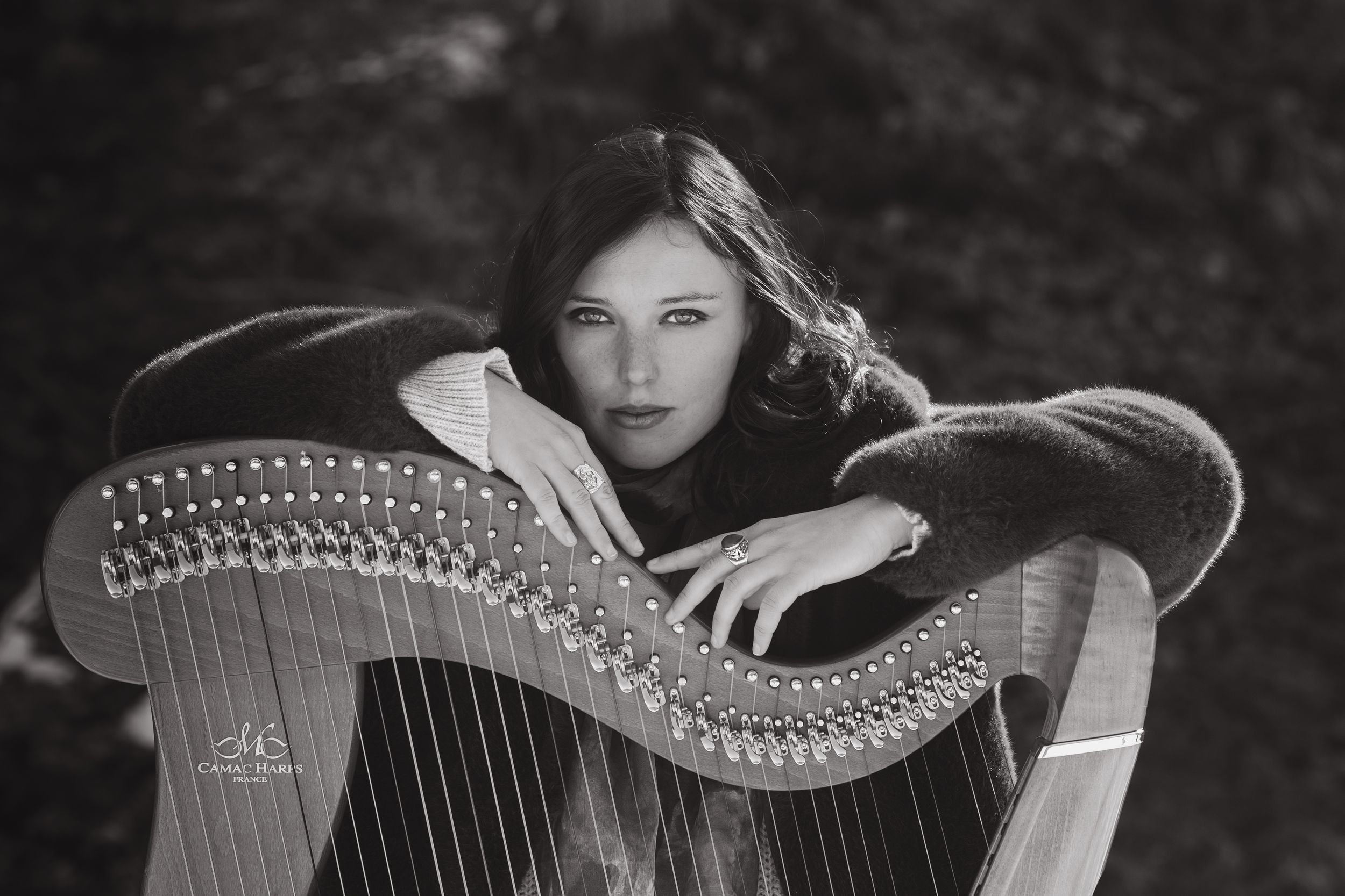 Dramatic black and white portrait with an elegant harp in a natural outdoor setting.
