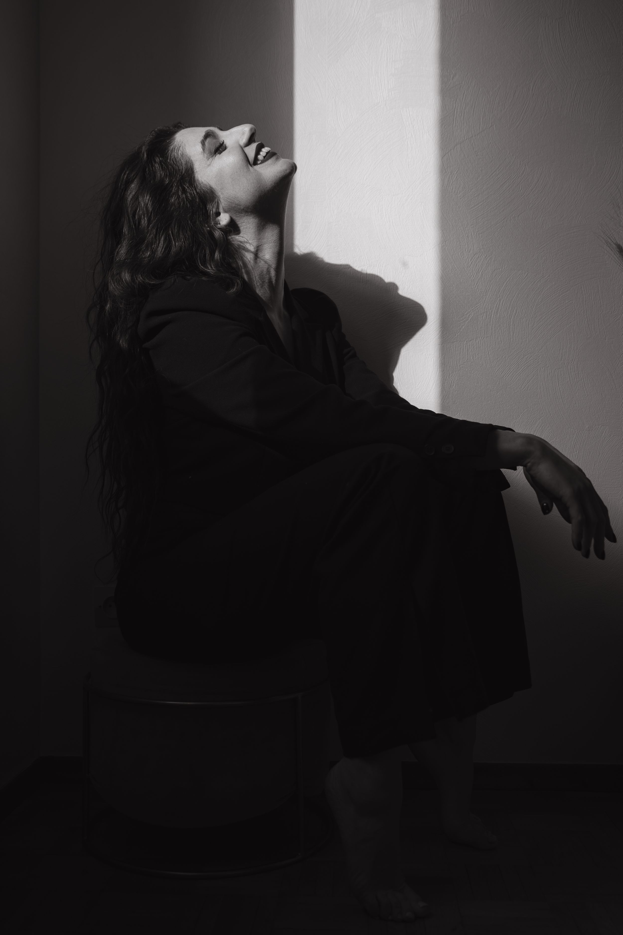 Dramatic black and white portrait with strong shadows against a white wall.