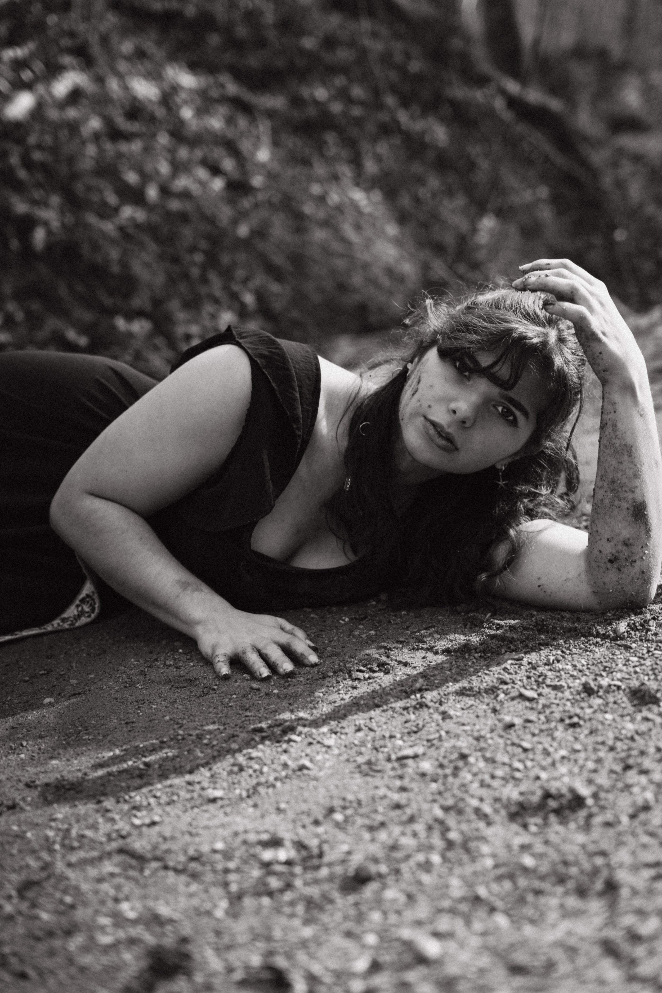 Black and white artistic portrait of someone lying on the ground in nature.