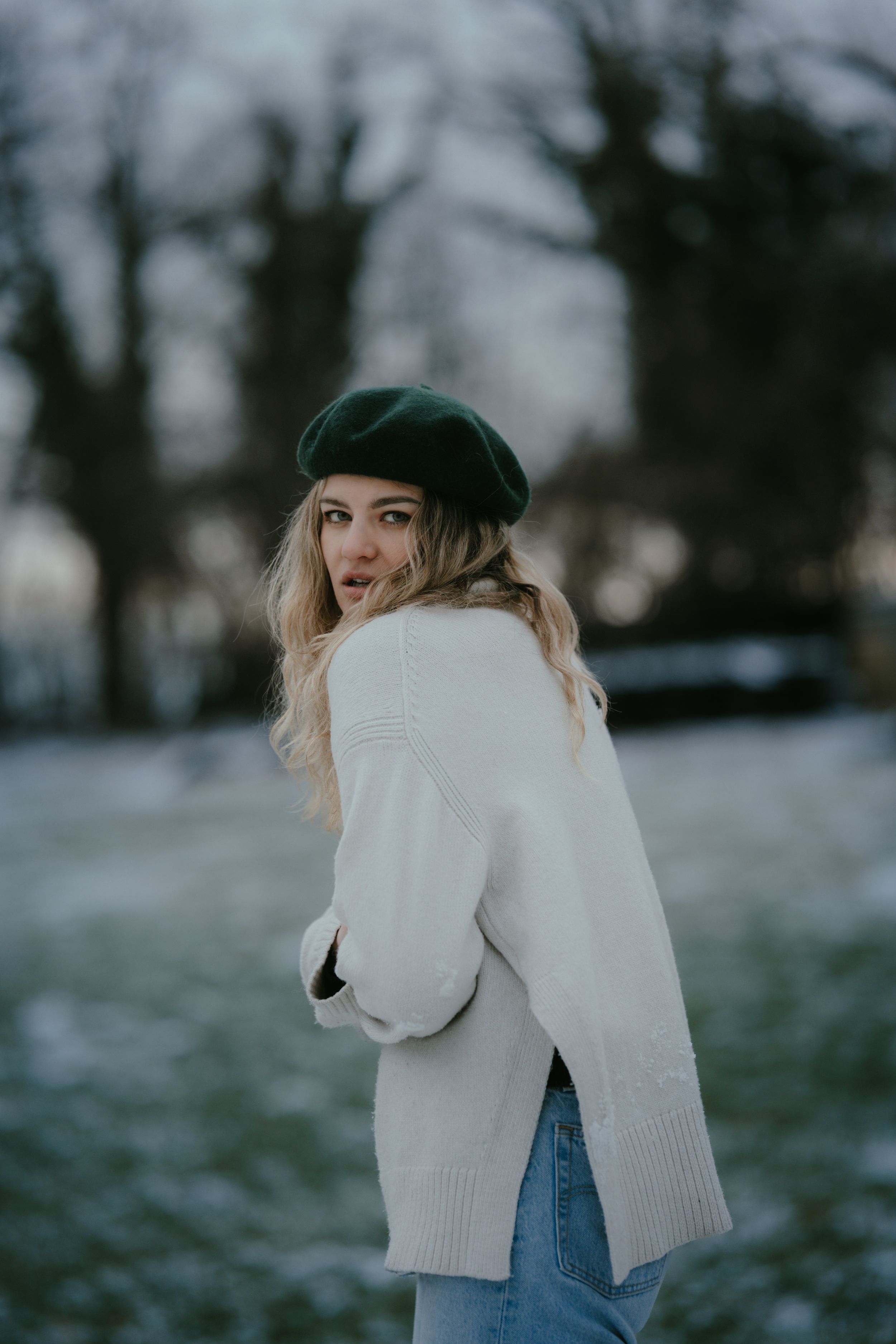 Winter portrait of a woman in white sweater and beret looking over her shoulder in frosty setting.