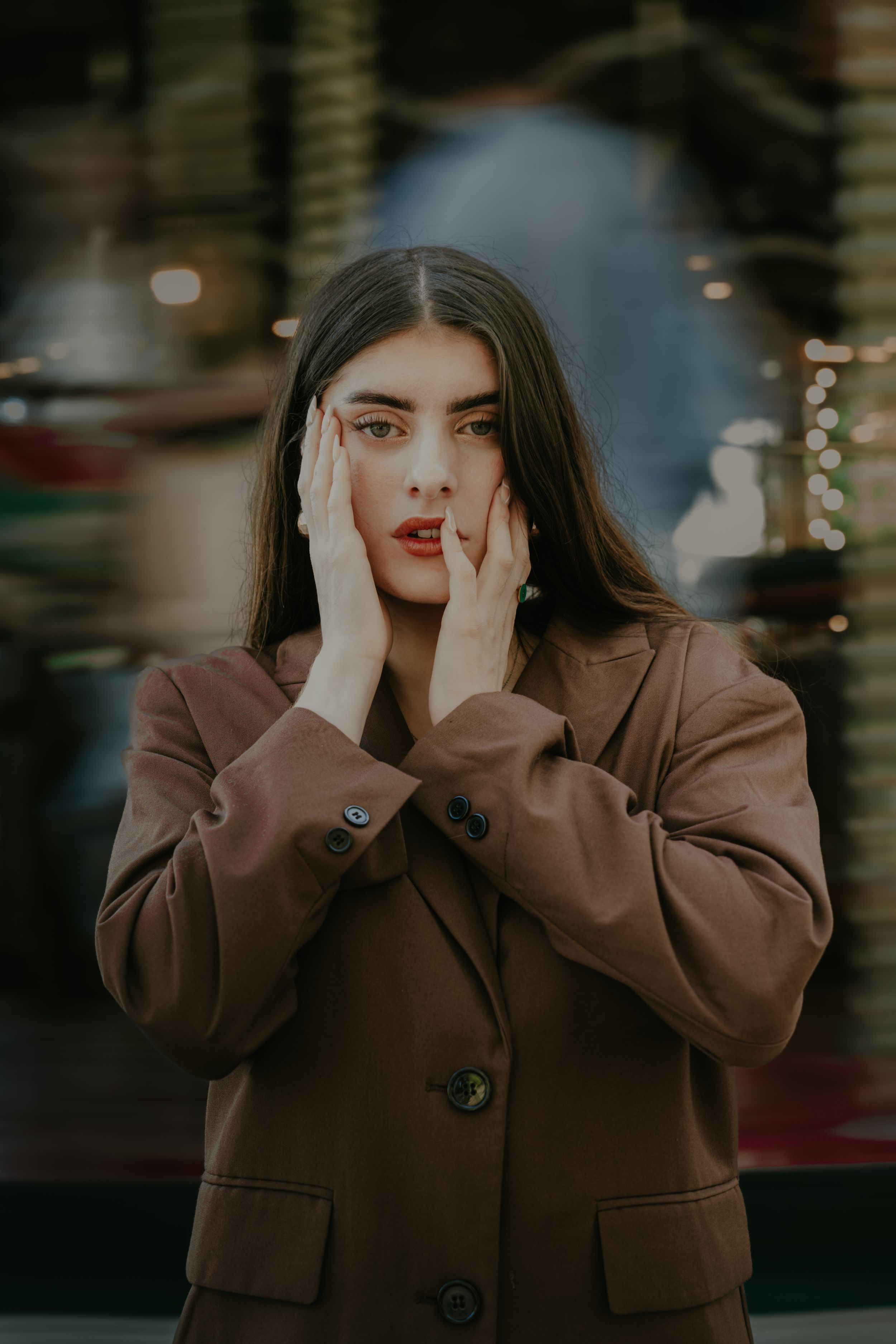 Portrait of someone in a brown coat with hands on face against blurred background.