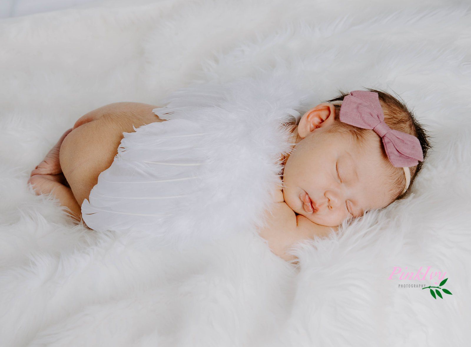 Newborn baby sleeping peacefully on white fur with pink headband.