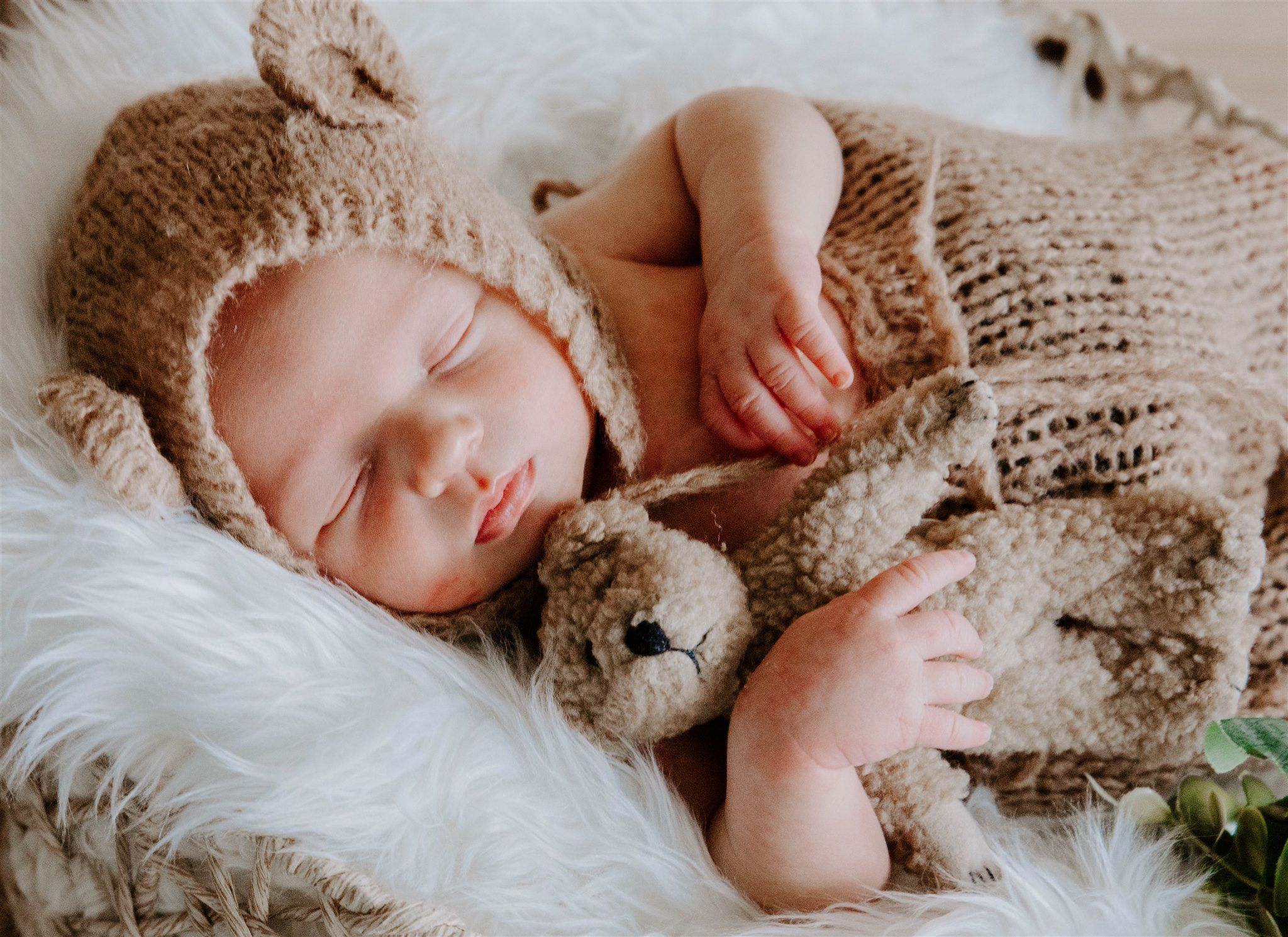 Sleeping newborn in knit outfit on soft white fur blanket.