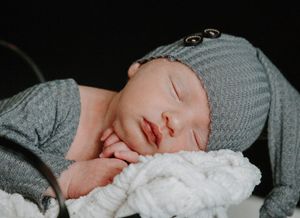 Sleeping newborn wrapped in white blanket against dark background.