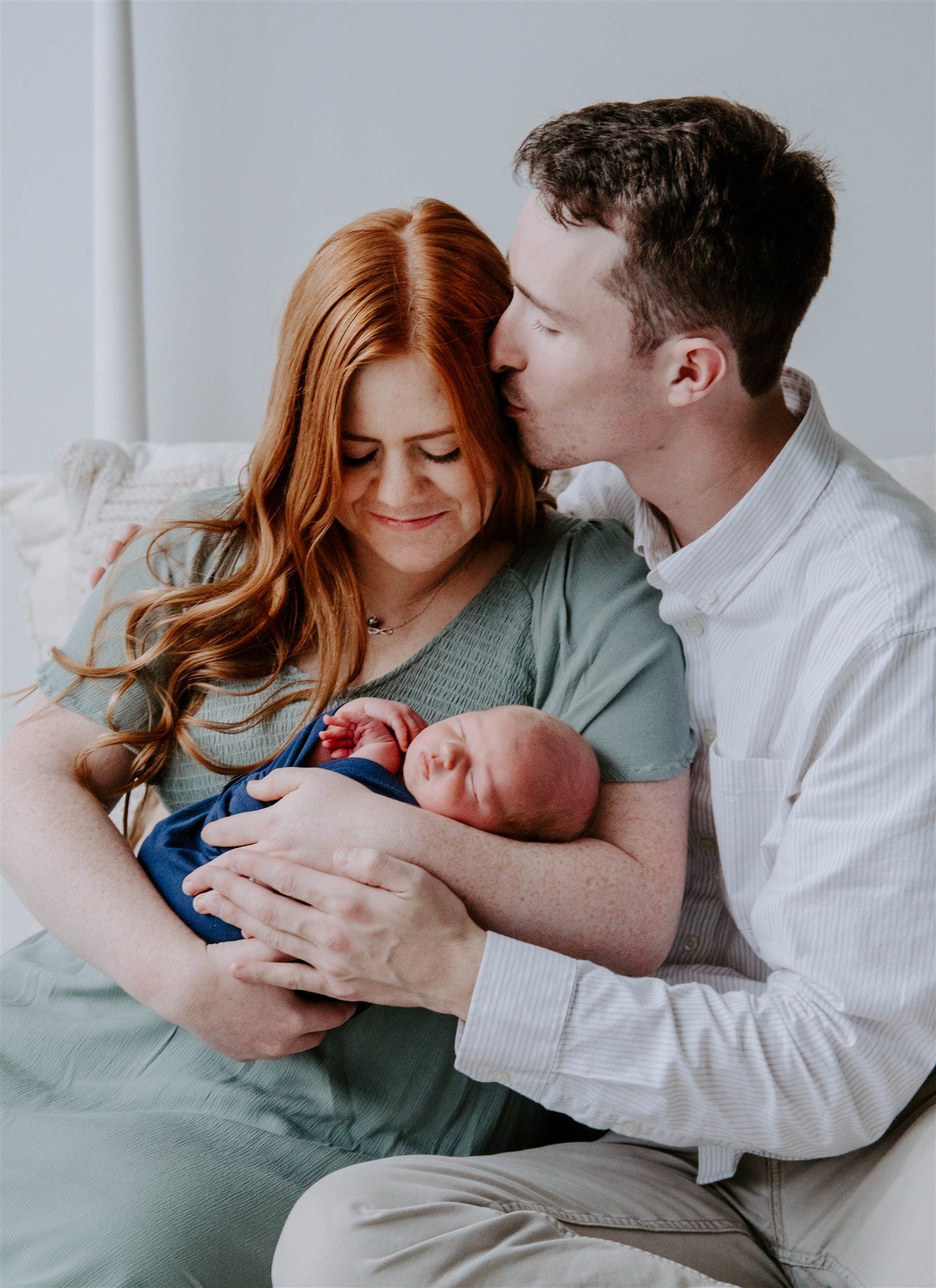 Tender family moment with newborn baby in blue outfit against light background.