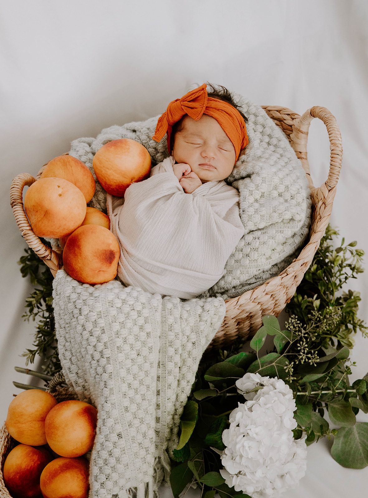Cozy newborn portrait with oranges and eucalyptus leaves in woven basket arrangement.
