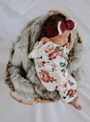 Newborn baby wearing floral print outfit rests on soft gray fur blanket in wicker basket.
