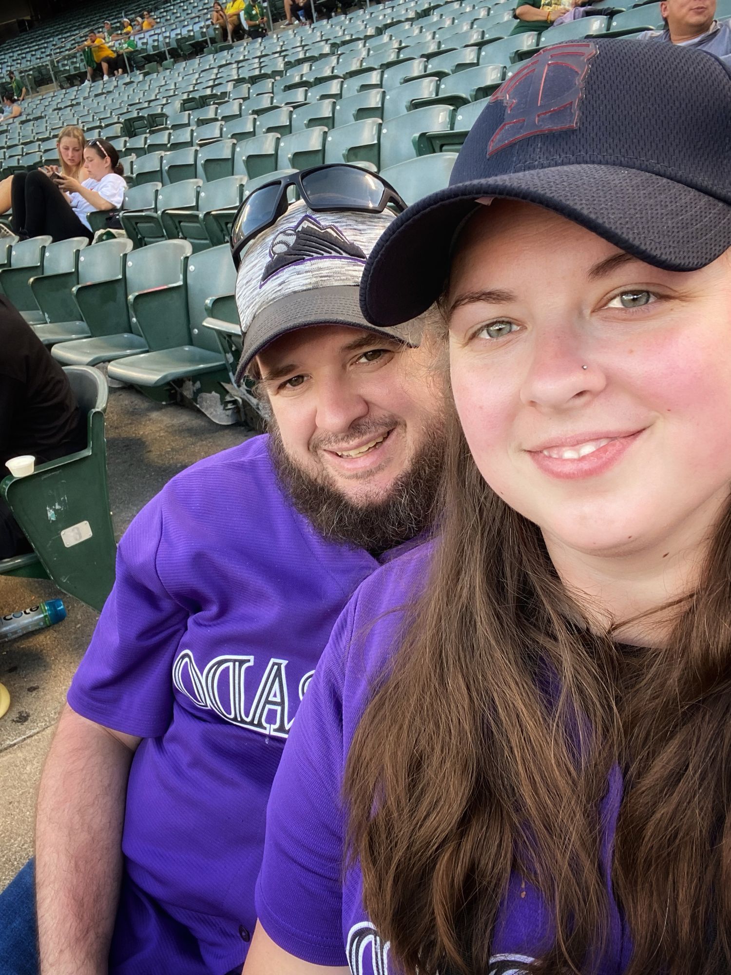 Baseball fans enjoying a game at stadium seats wearing purple team apparel.
