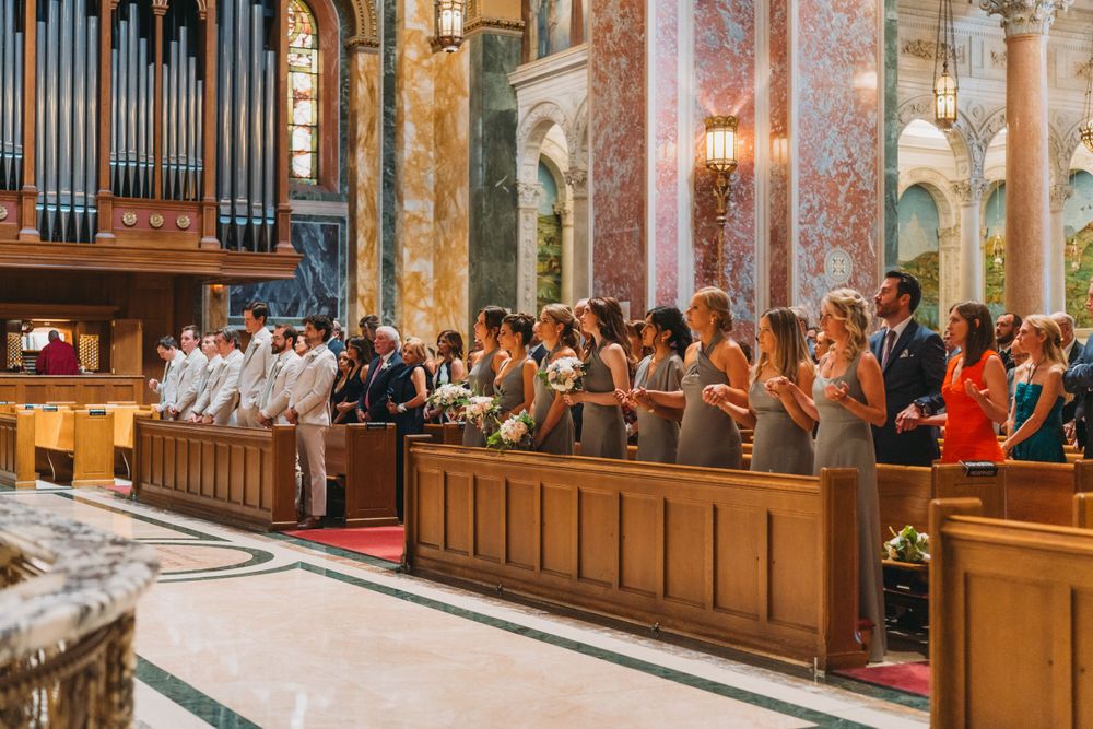 Wide angle view of wedding guests seated in wooden pews inside a grand cathedral.