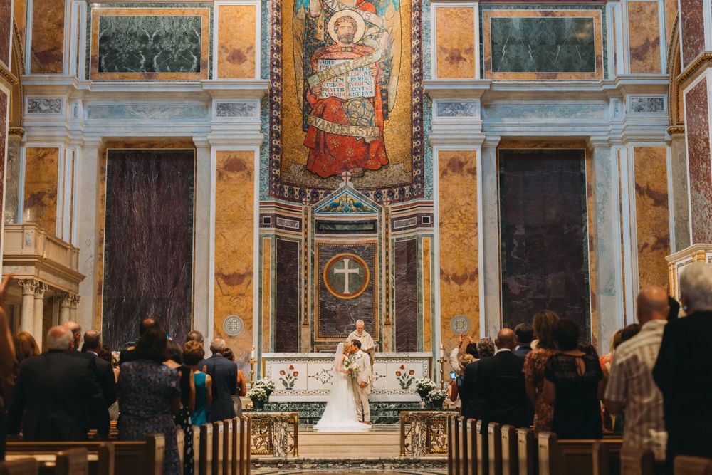 Panoramic view of an elegant church interior with ornate frescoes and marble columns during a wedding ceremony.