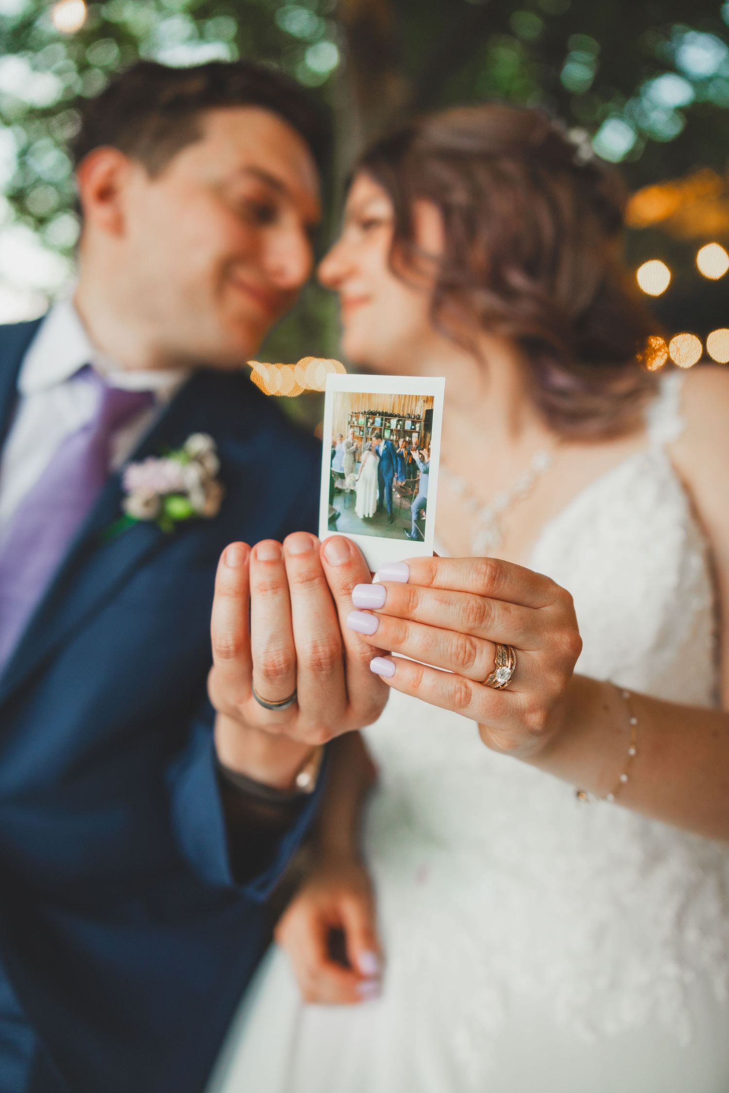 Wedding couple holding polaroid photo with string lights and garden backdrop.