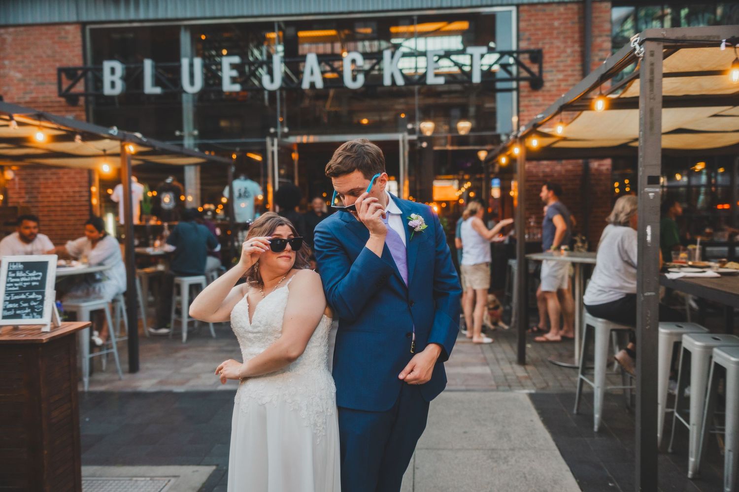 Couple enjoying moment outside Blue Jacket restaurant with string lights overhead.