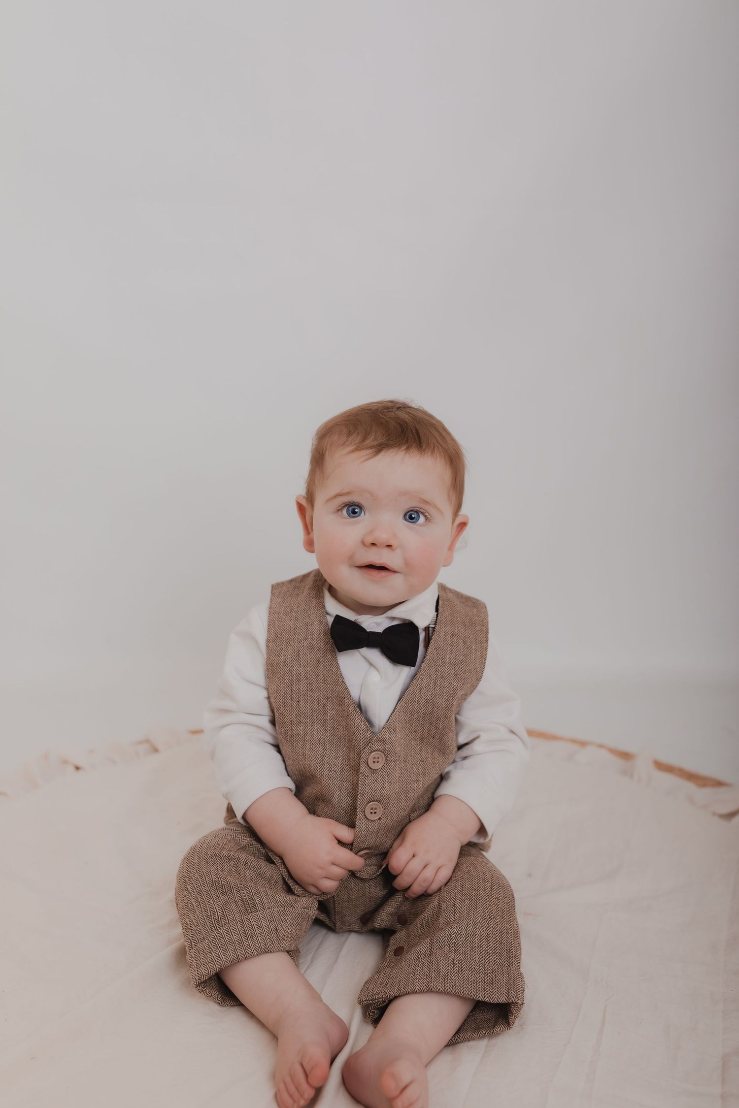Infant in brown vest and bowtie outfit sitting on cream coloured backdrop. Photographer. Hull. East Yorkshire. Photography