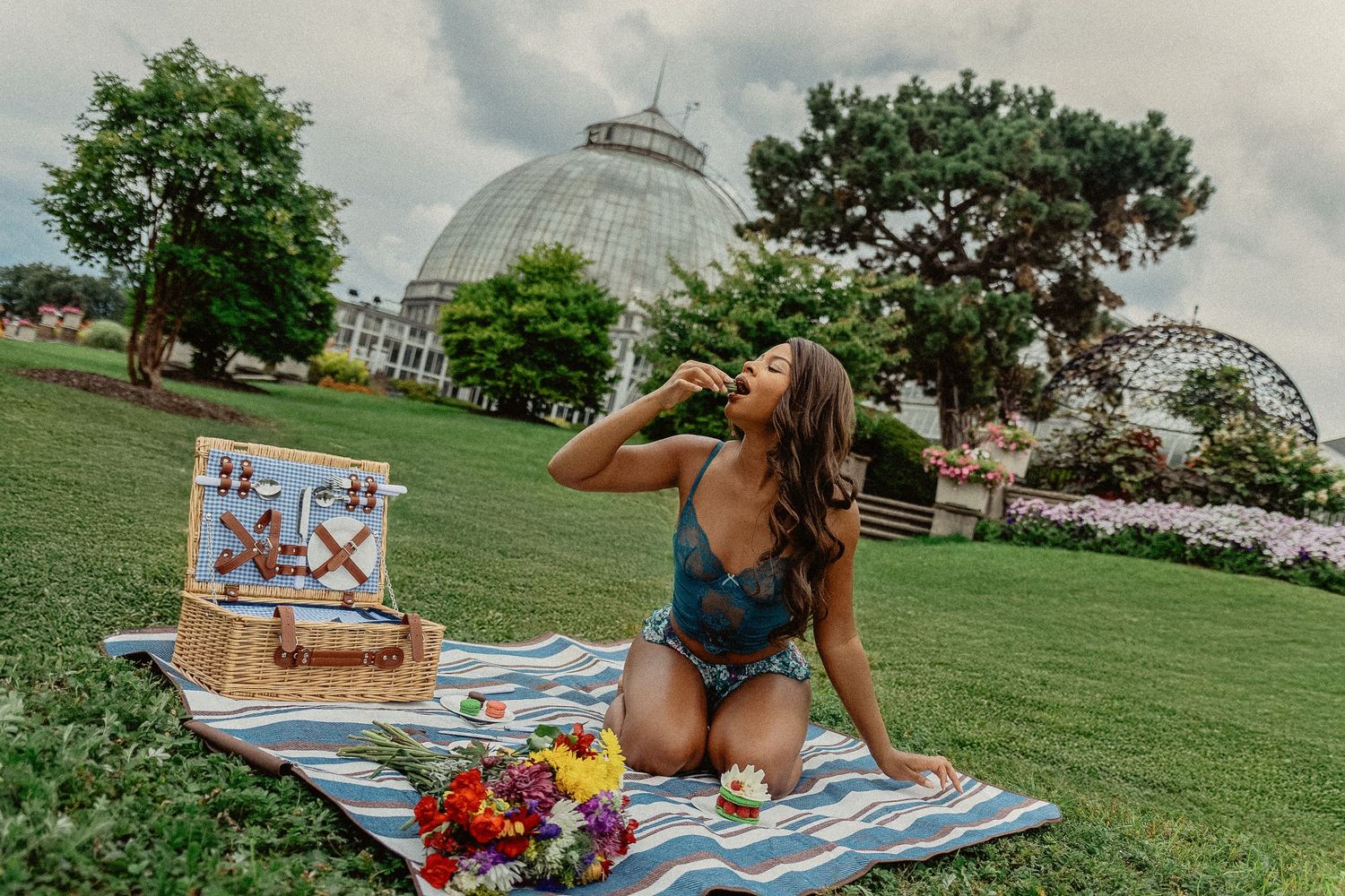 Summer picnic on the lawn in front of glass conservatory domes with picnic basket, blanket and colorful flowers.
