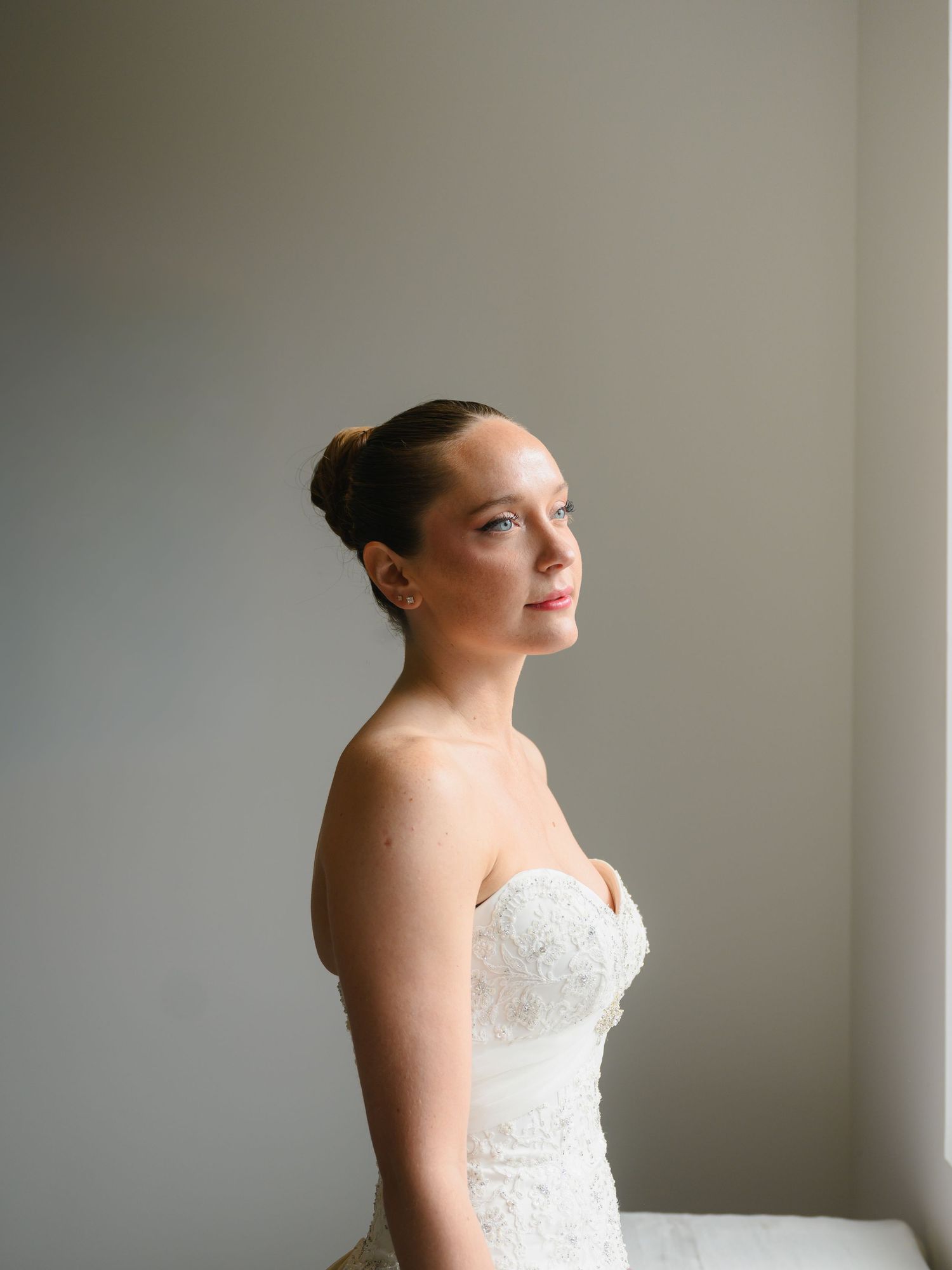 Elegant bride in strapless lace wedding gown poses gracefully in soft natural light.