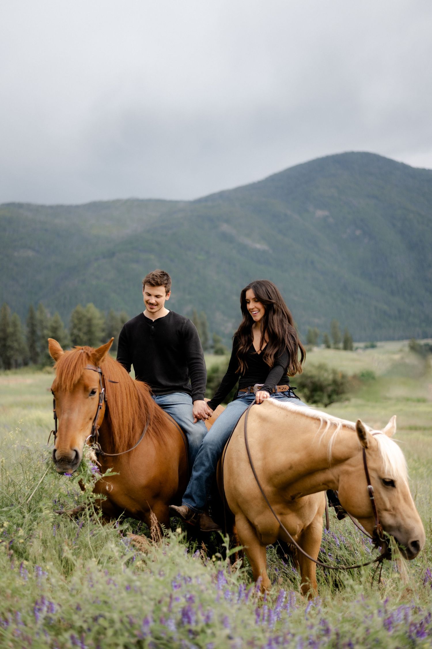 couple riding their horses through  mountains