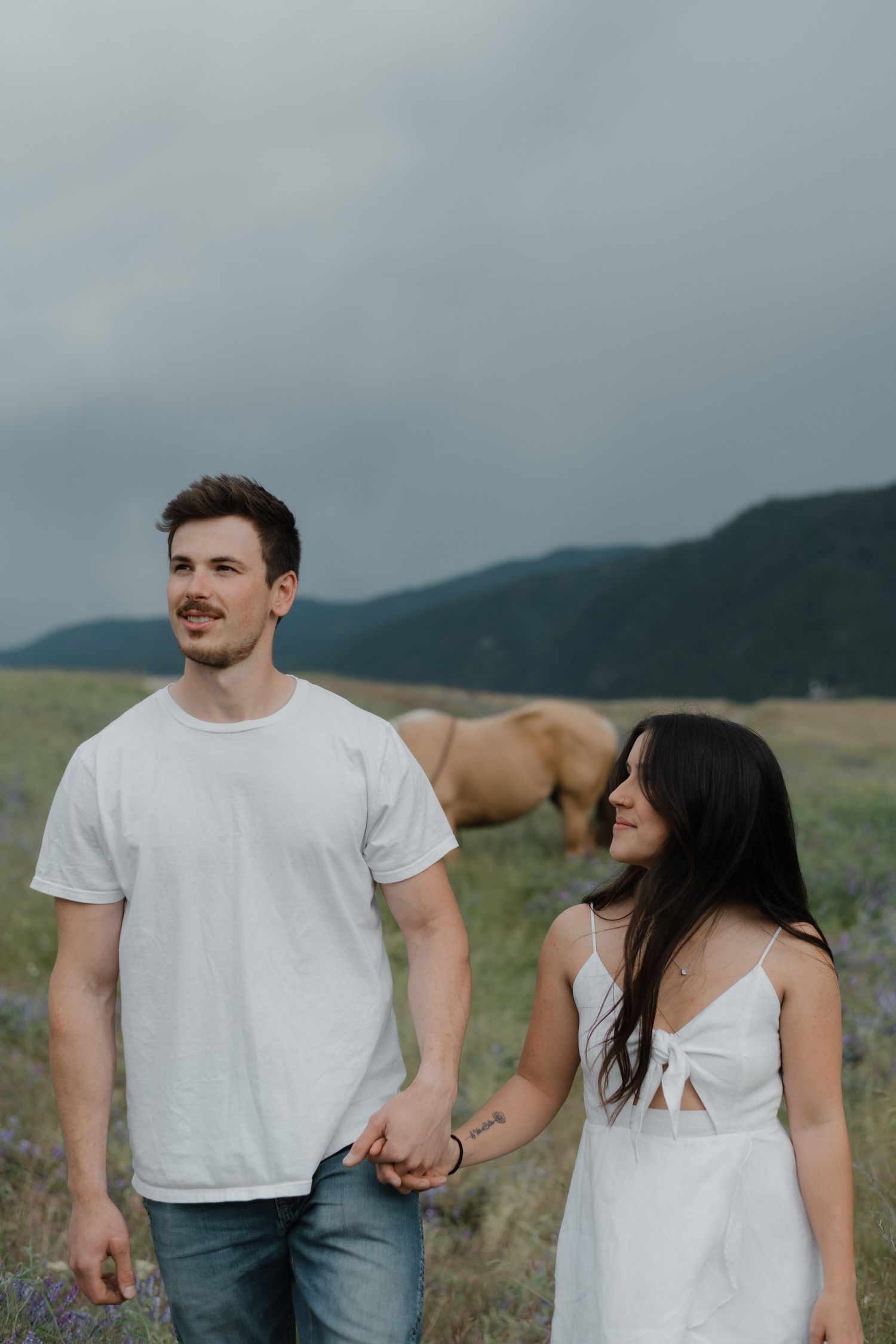 couple walking and holding hands with horses behind them