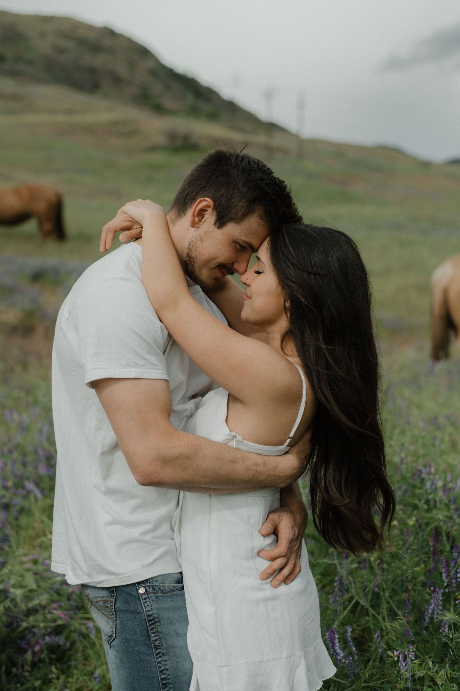 couple hugging with horses behind them