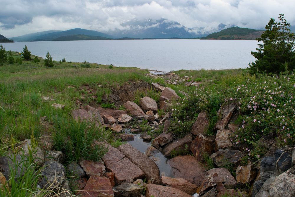 Rocky creek bed leads to a mountain lake surrounded by misty peaks.