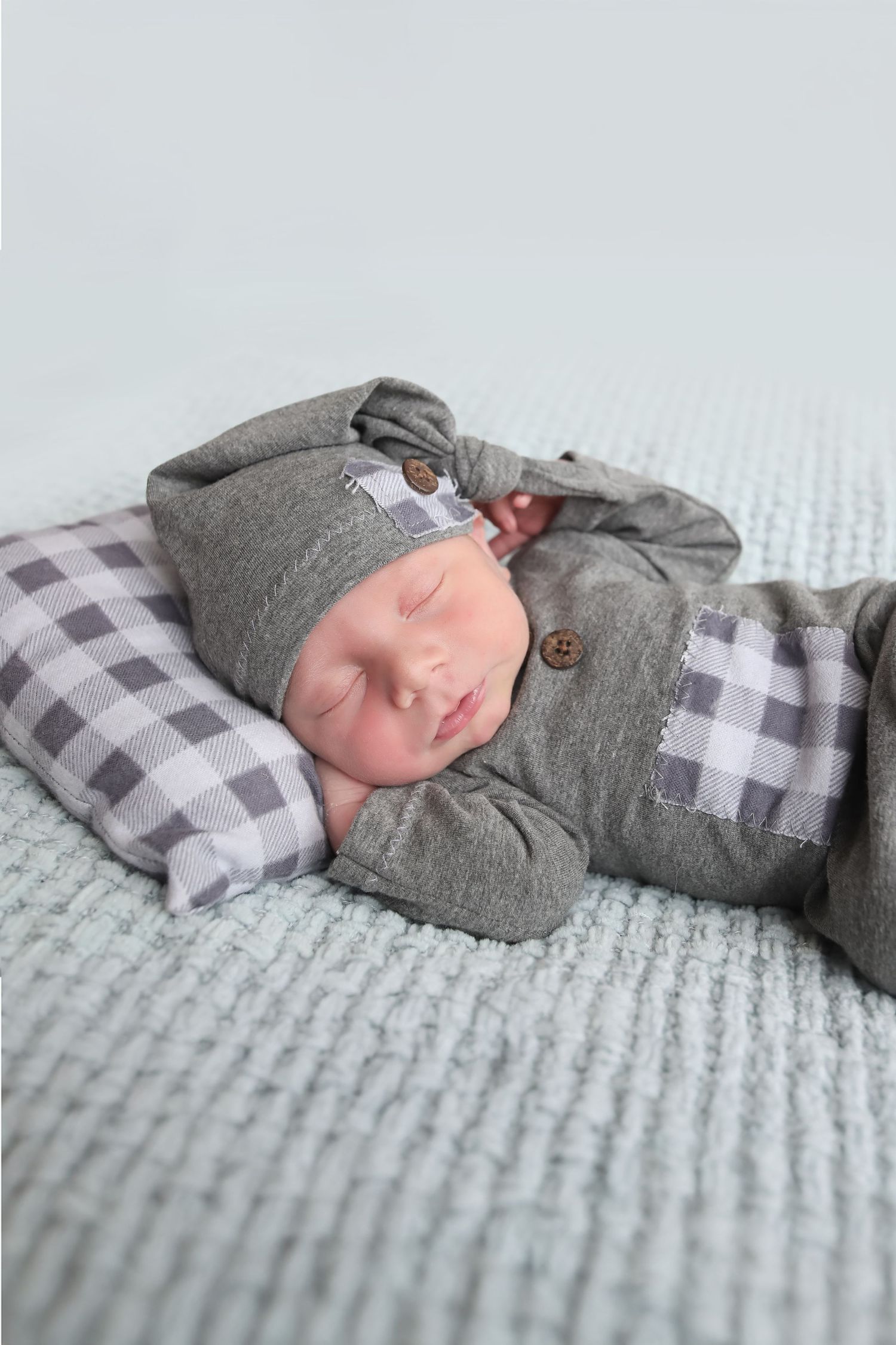 Sleeping infant wearing grey button cardigan on buffalo check blanket.