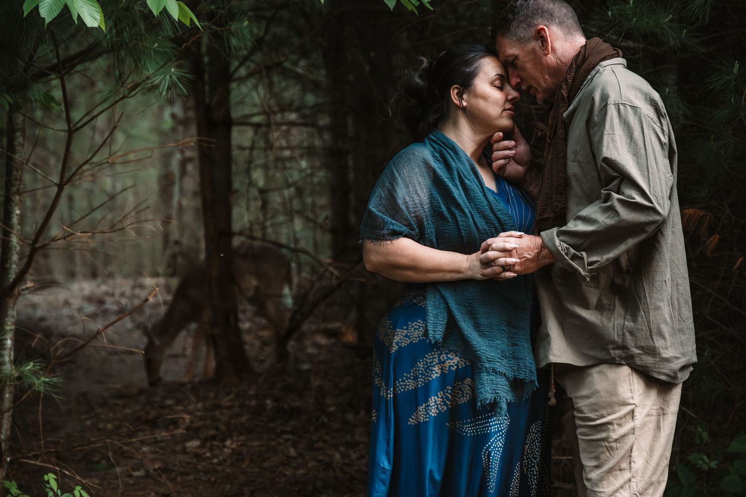 Couple sharing a tender romantic moment in a lush forest setting, holding hands and touching foreheads.