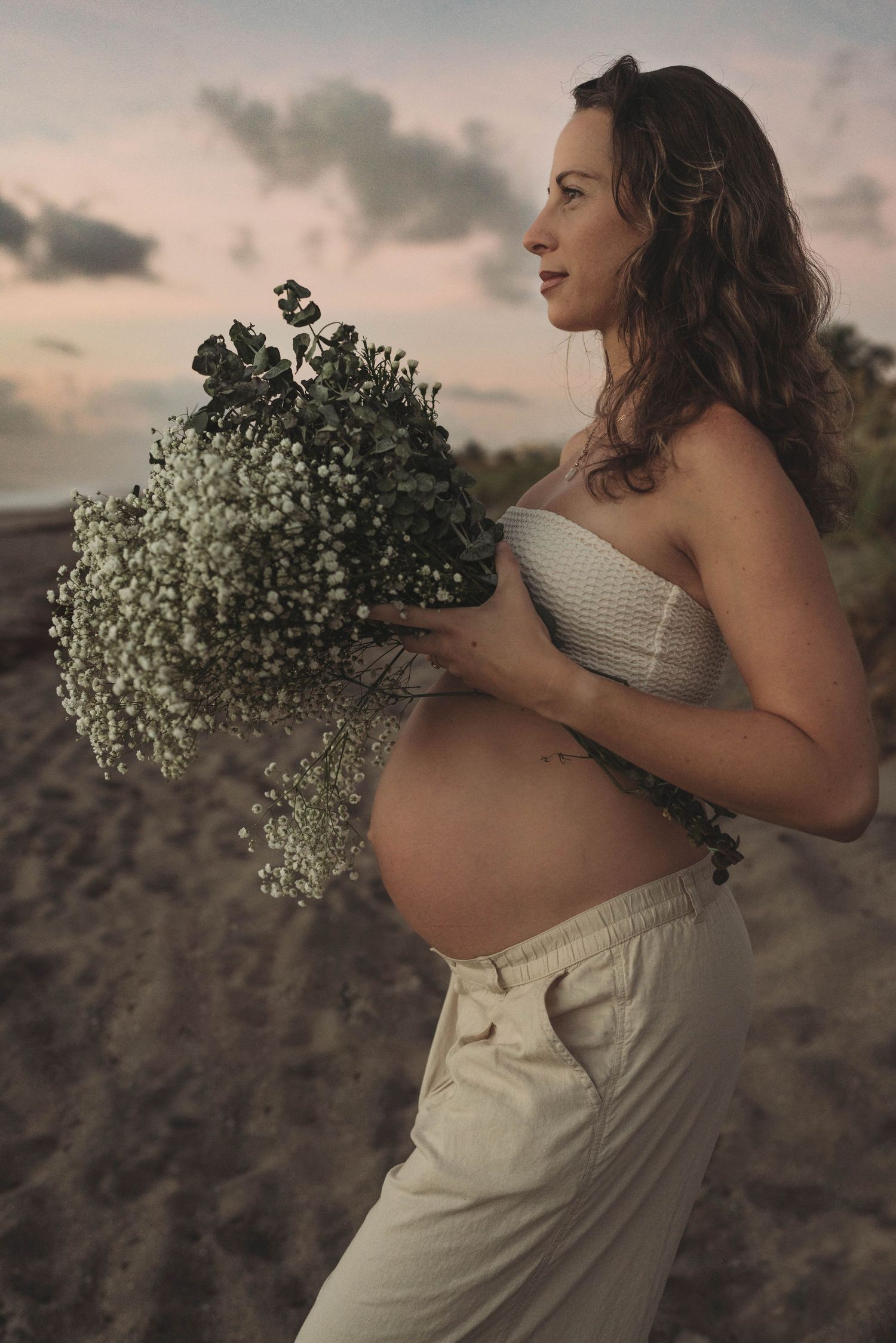 Maternity portrait featuring baby bump and delicate bouquet of baby's breath flowers.