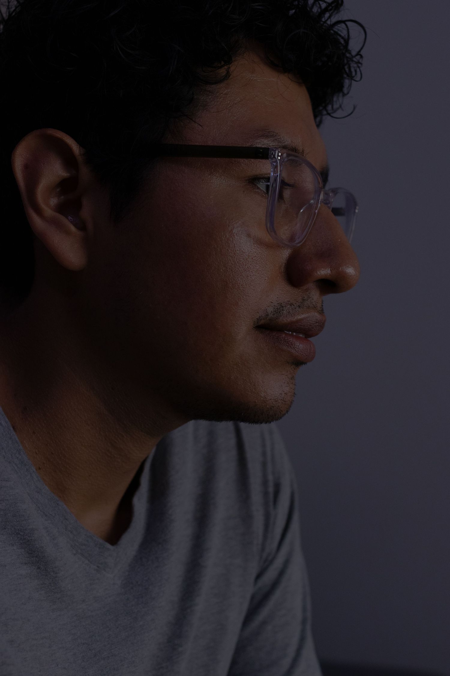 A side profile view of someone wearing glasses and a gray t-shirt in moody lighting.