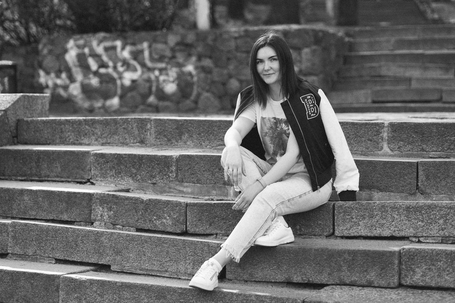 Vilnius portrait photographer Kateryna Tiupa (Katelavey) sits on the steps in jeans and a bomber jacket