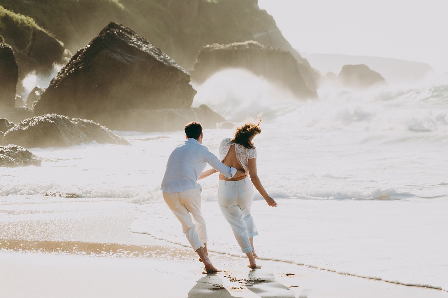 Pareja corriendo por la orilla del mar durante una sesión de preboda en la playa de Asturias