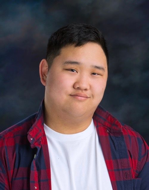 Portrait of person in red and navy plaid shirt against dark backdrop.