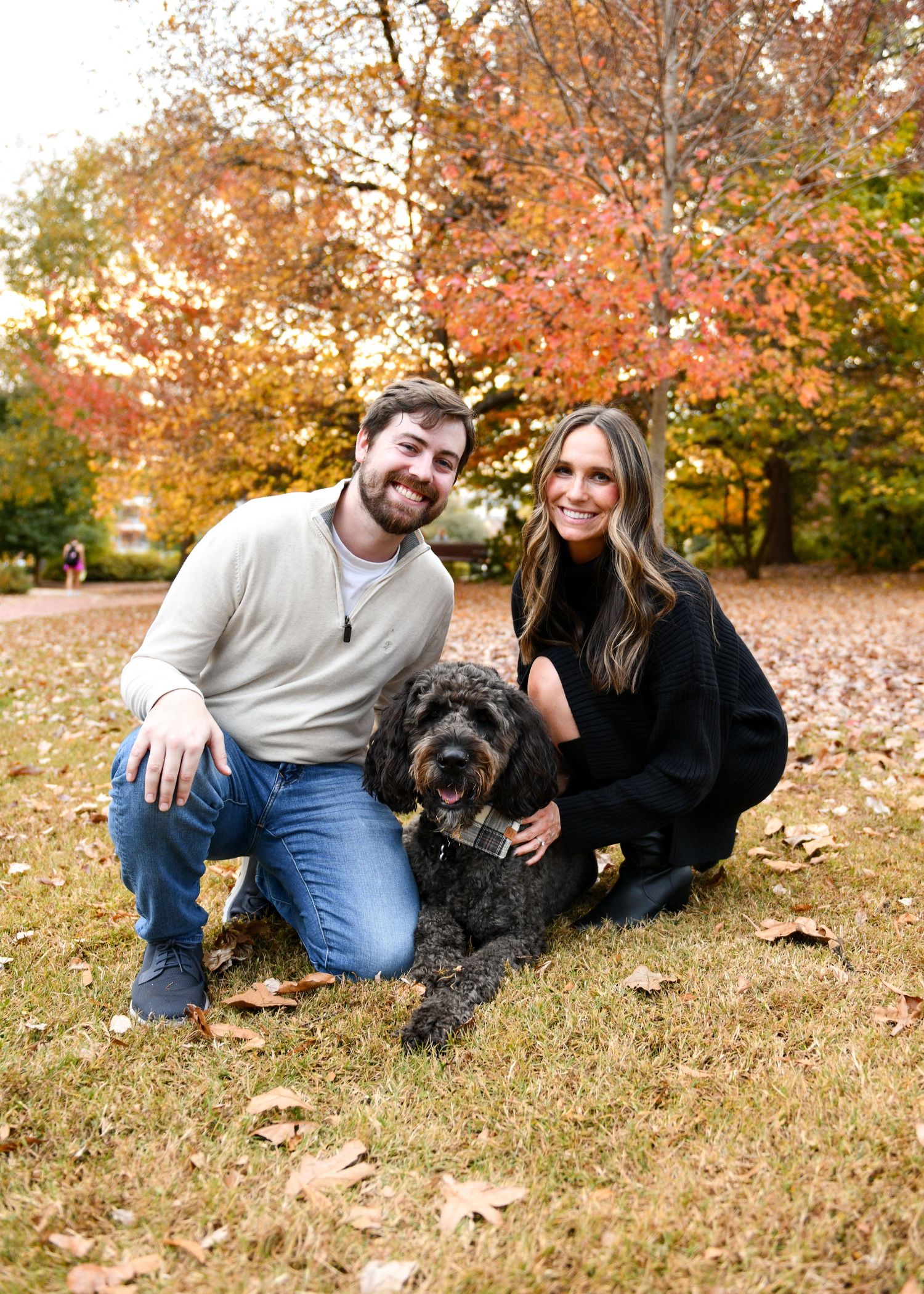 Couple with their black dog sitting on fallen autumn leaves in the park.