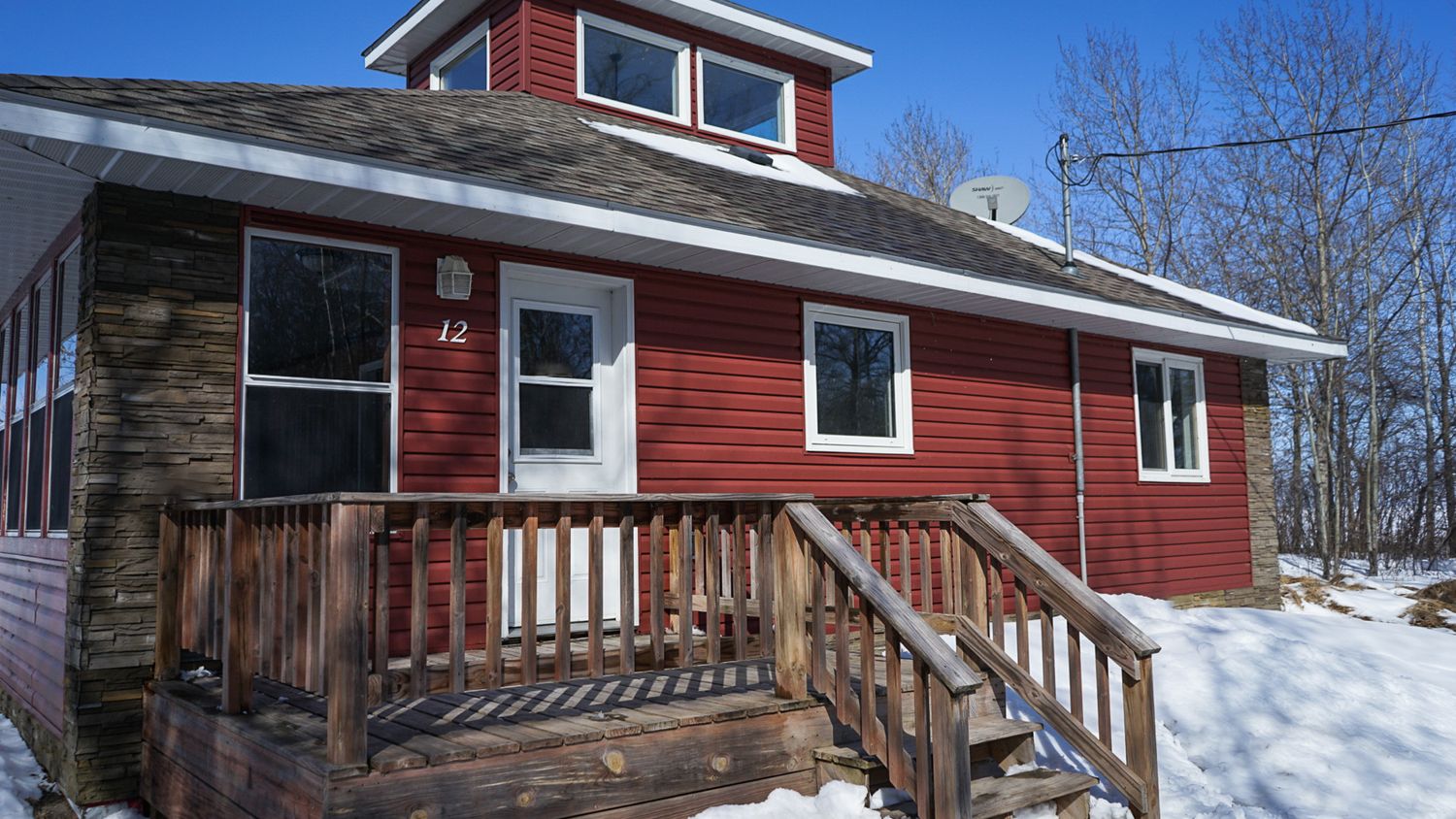 Red wooden cabin with white trim and snow-covered roof in winter setting.