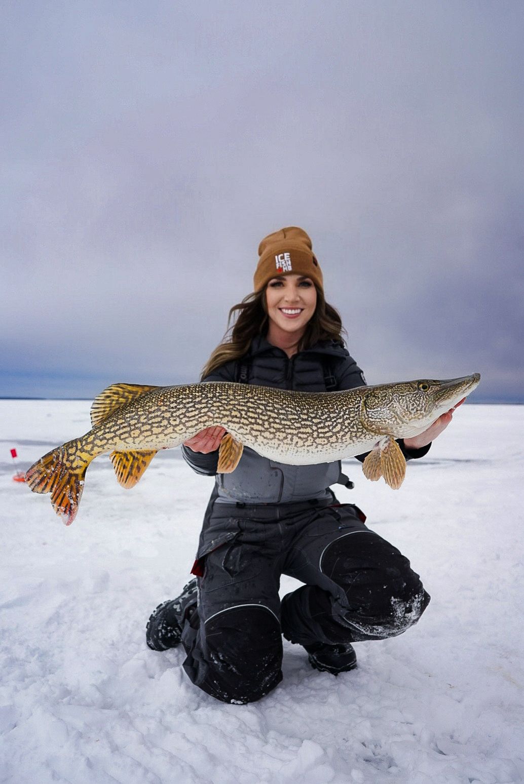 Ice fishing catch of a large northern pike displayed on snowy surface.
