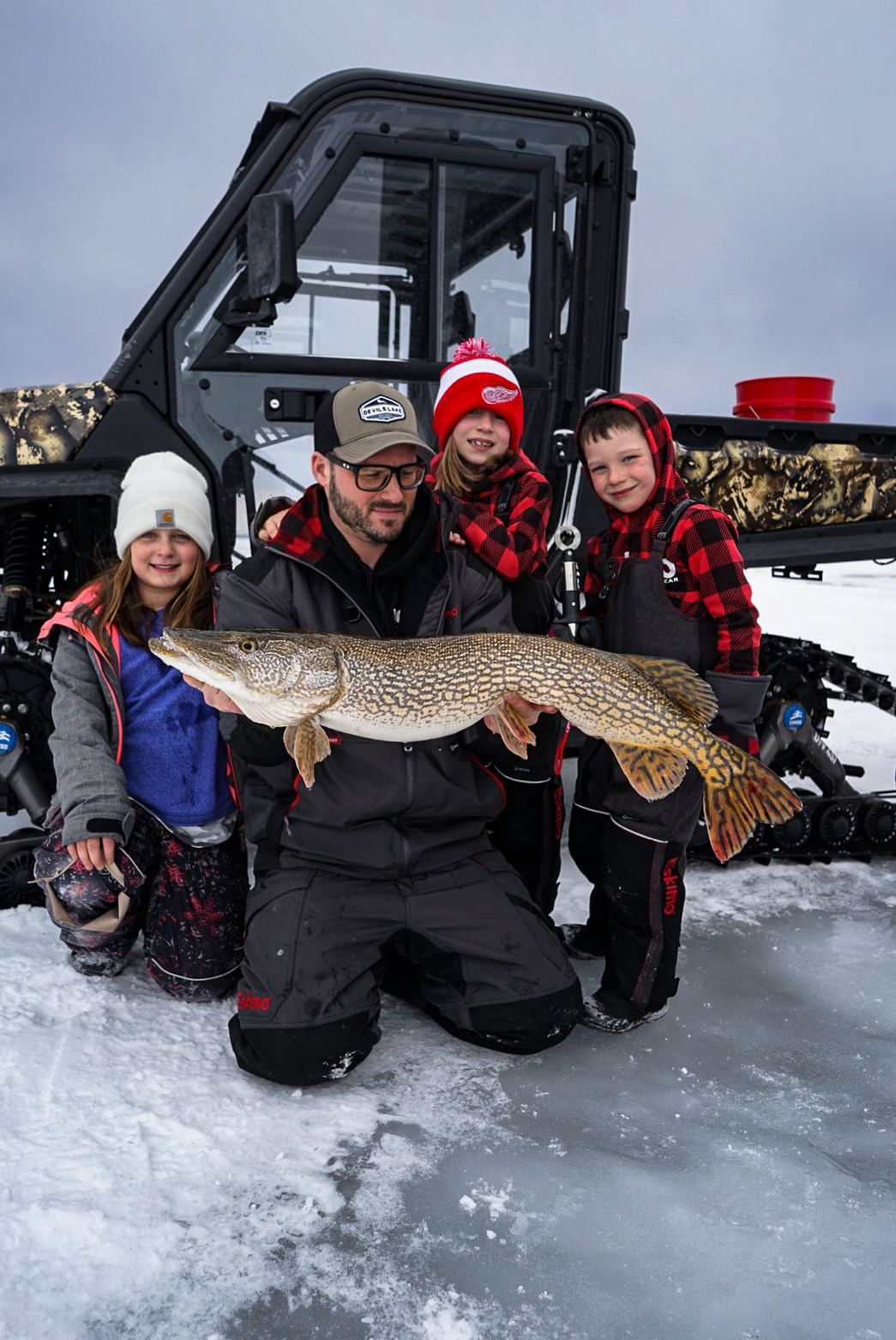 Group displaying their caught northern pike while ice fishing next to a snowmobile.