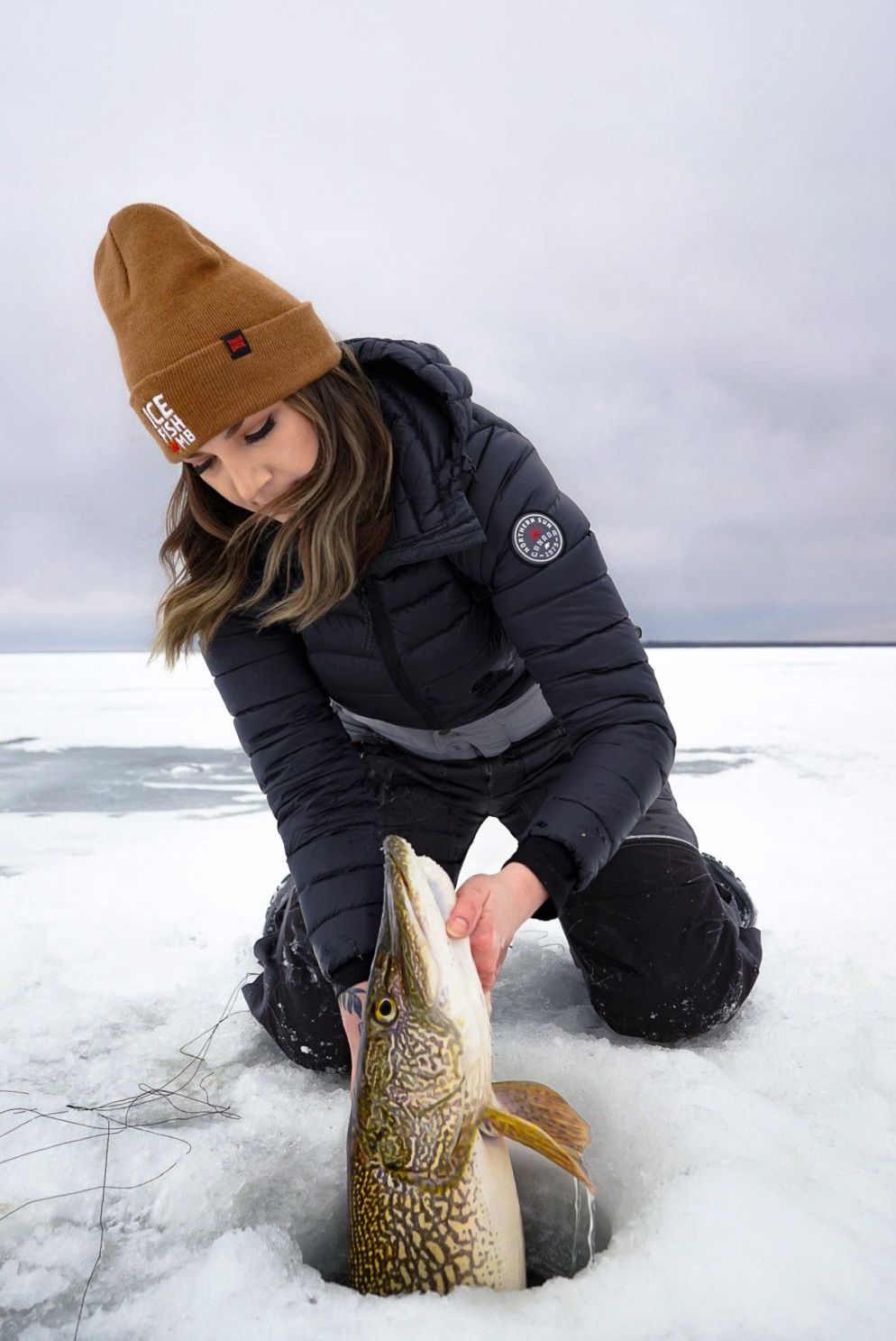 Winter angler releasing a northern pike back through an ice fishing hole.