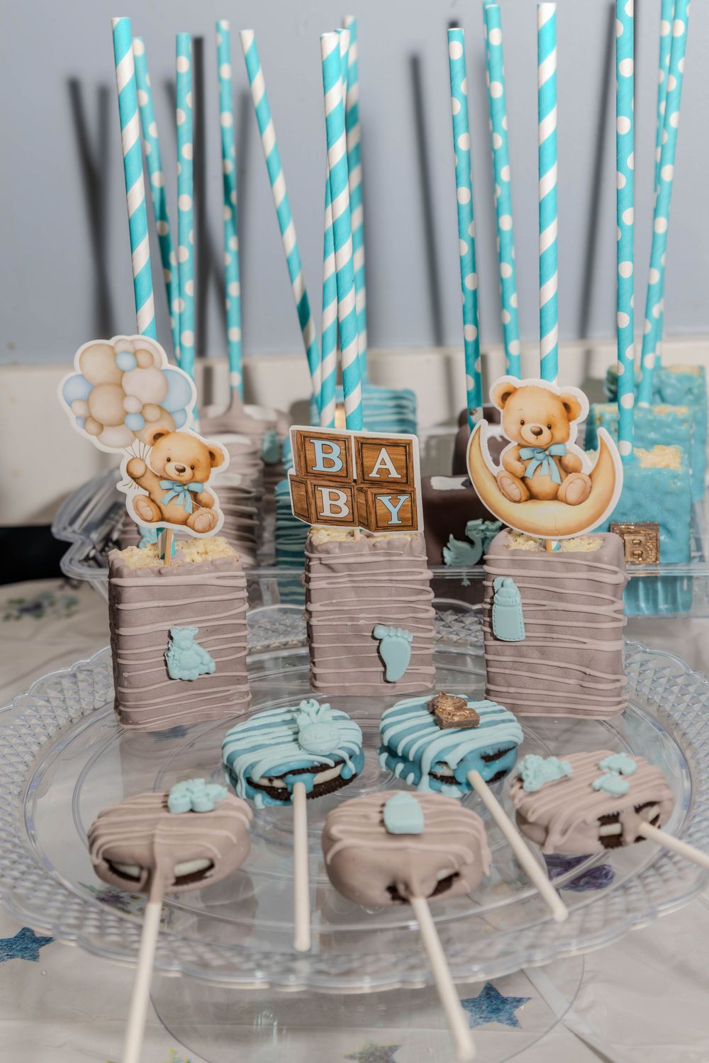 Blue and white striped paper straws with teddy bear cake pops decorated in pastel colors.