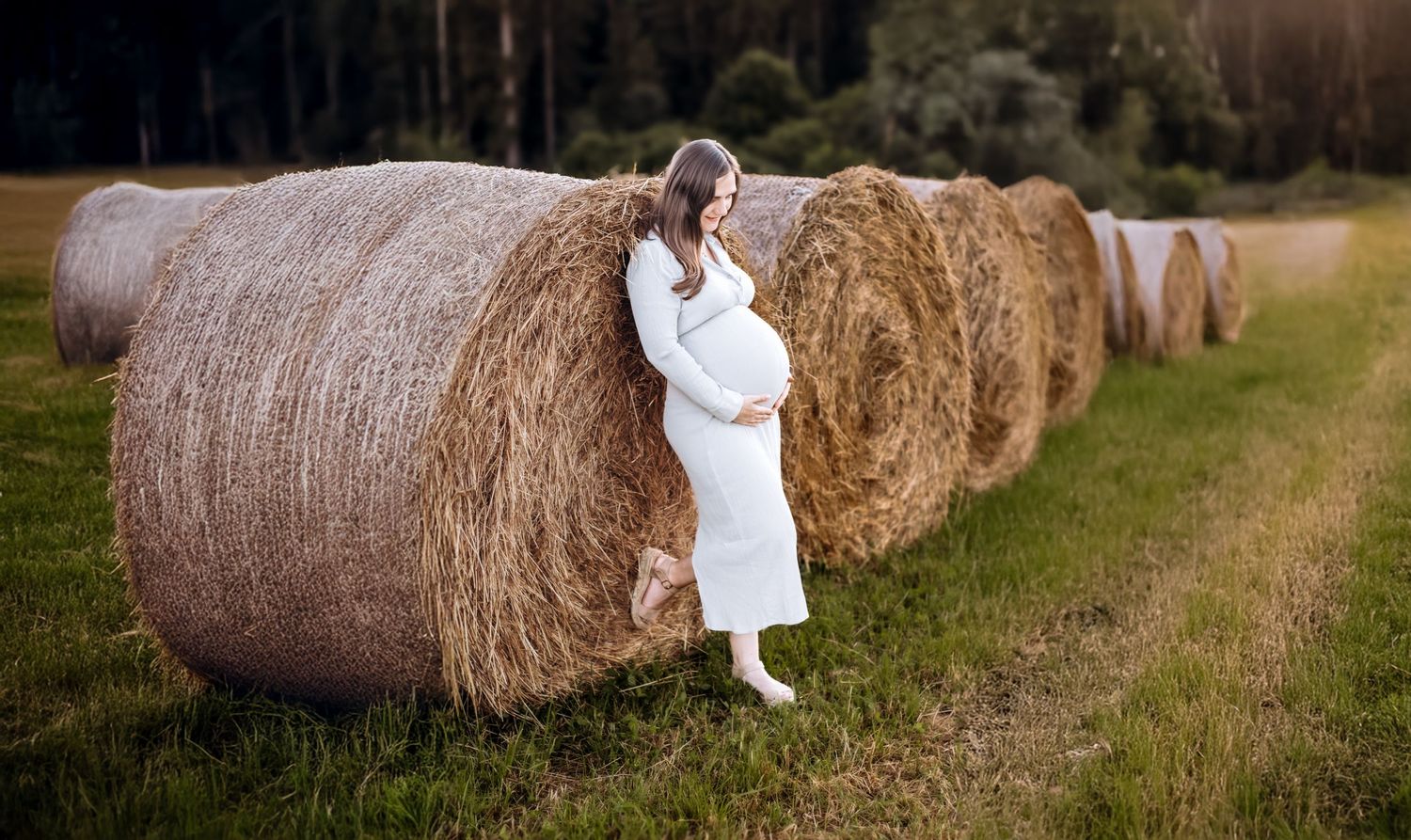 Schwangere Frau in einem fließenden Kleid, fotografiert vor einer malerischen Feldkulisse in Kaiserslautern.