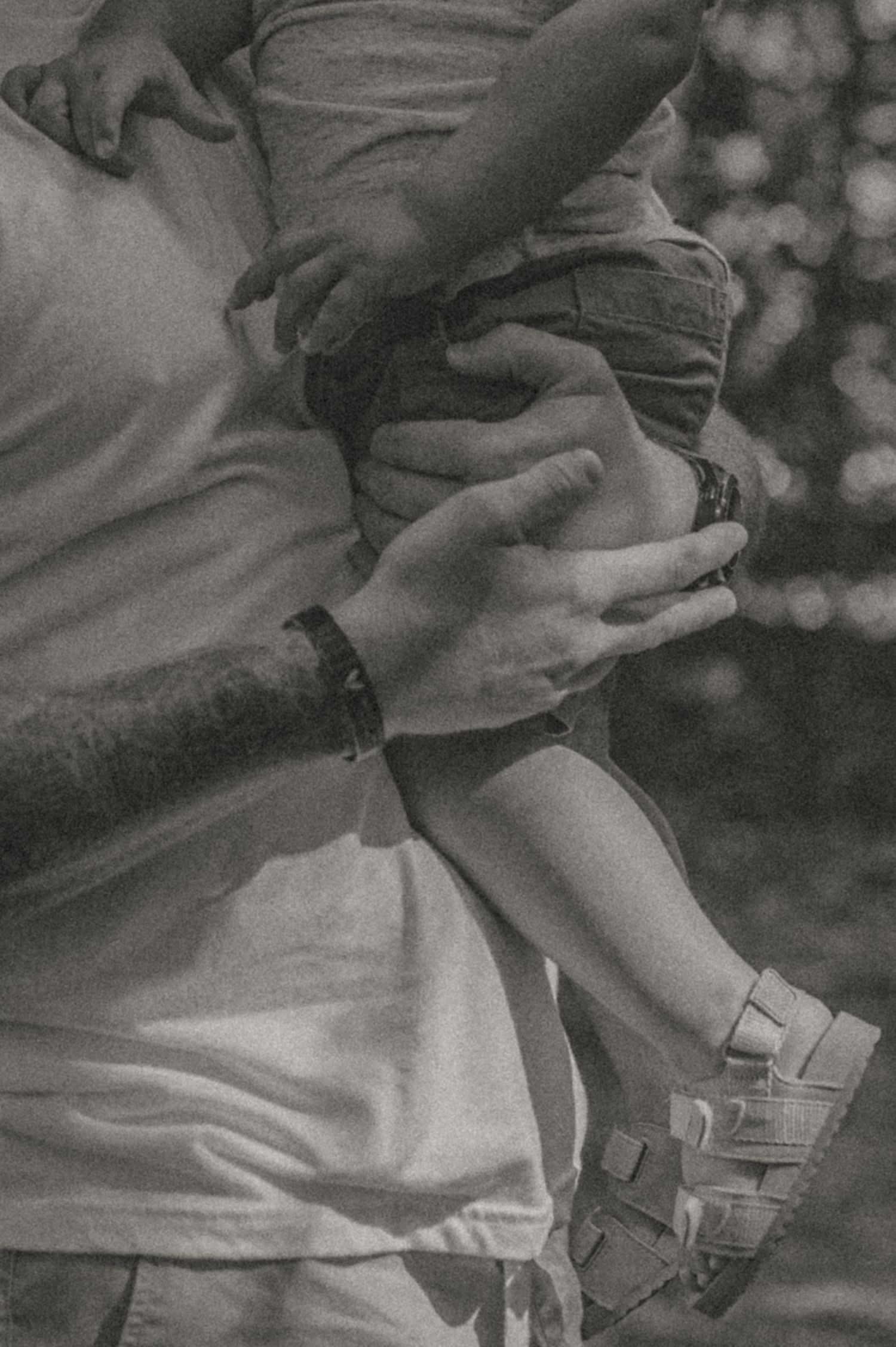 Black and white photo by Samantha Campbell imagery showing hands holding a small foot wearing sandals in a tender parental moment.