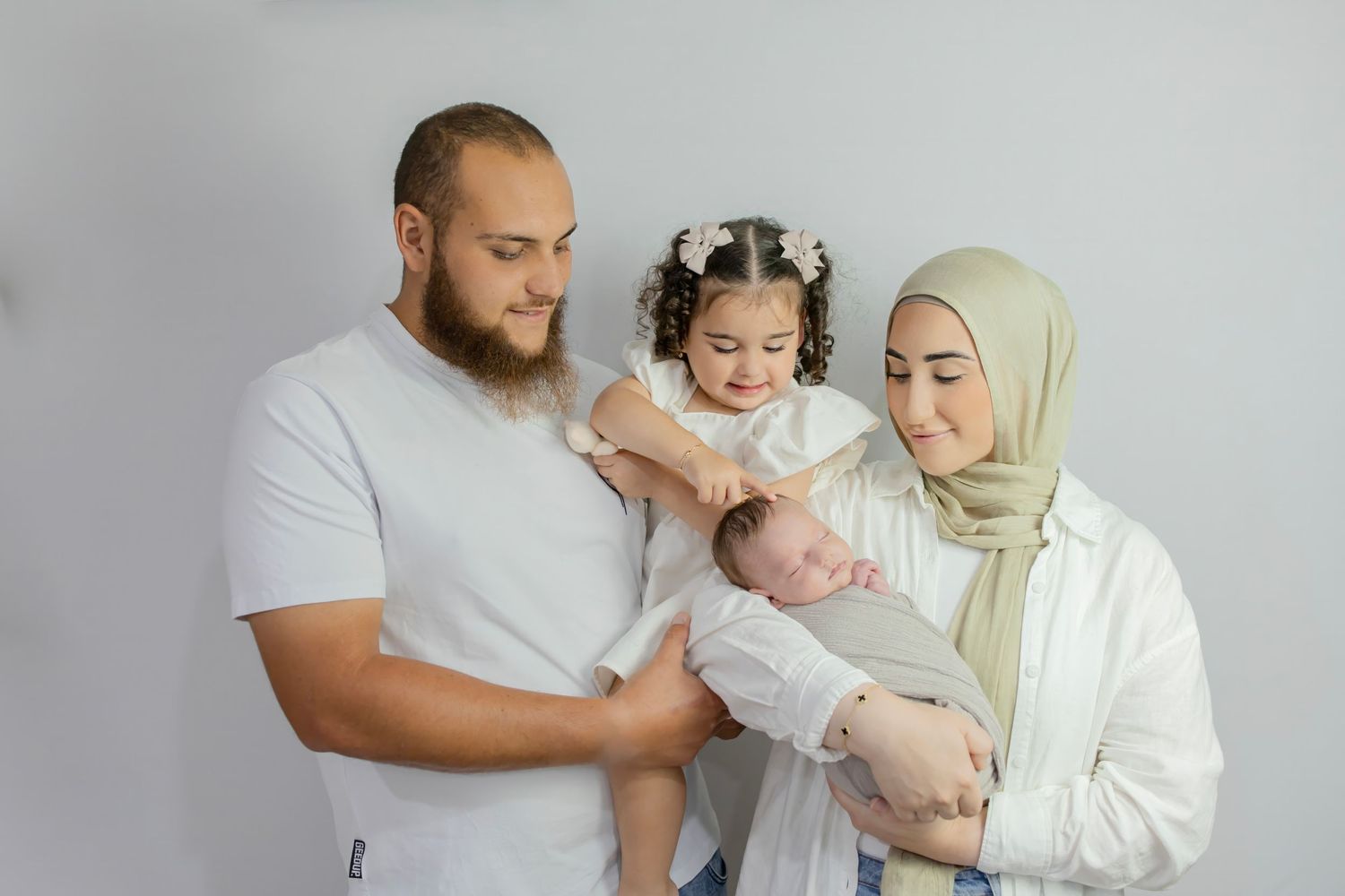 Muslim family with father, toddler daughter, and mother in hijab holding newborn.
