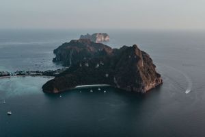 Aerial view of a rocky island surrounded by blue ocean waters with boats anchored along its coastline.