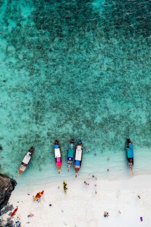 Aerial view of longtail boats moored along white sand beach with crystal clear turquoise waters.