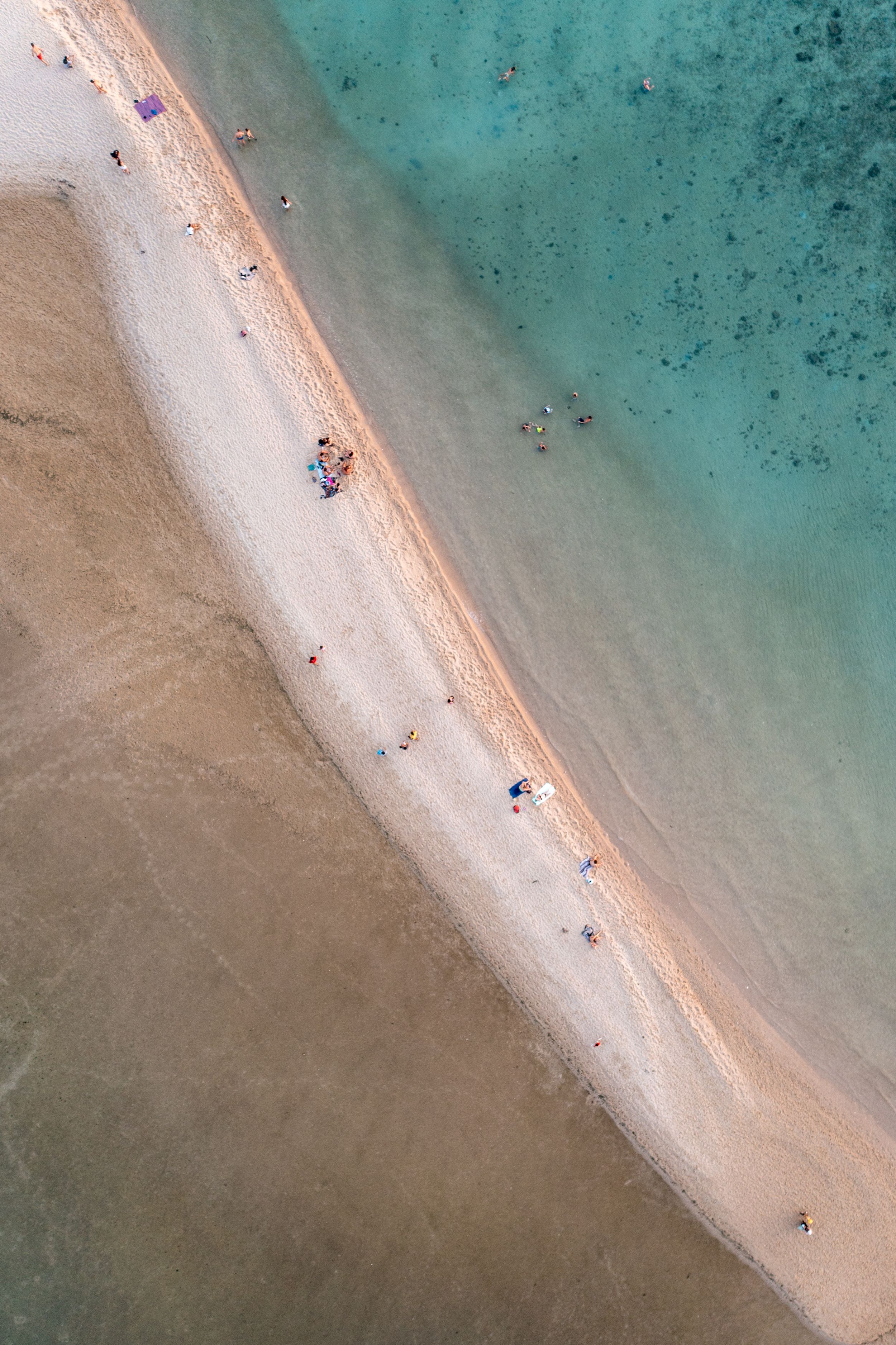 Aerial view of a curved sandy beach meeting turquoise waters from above.