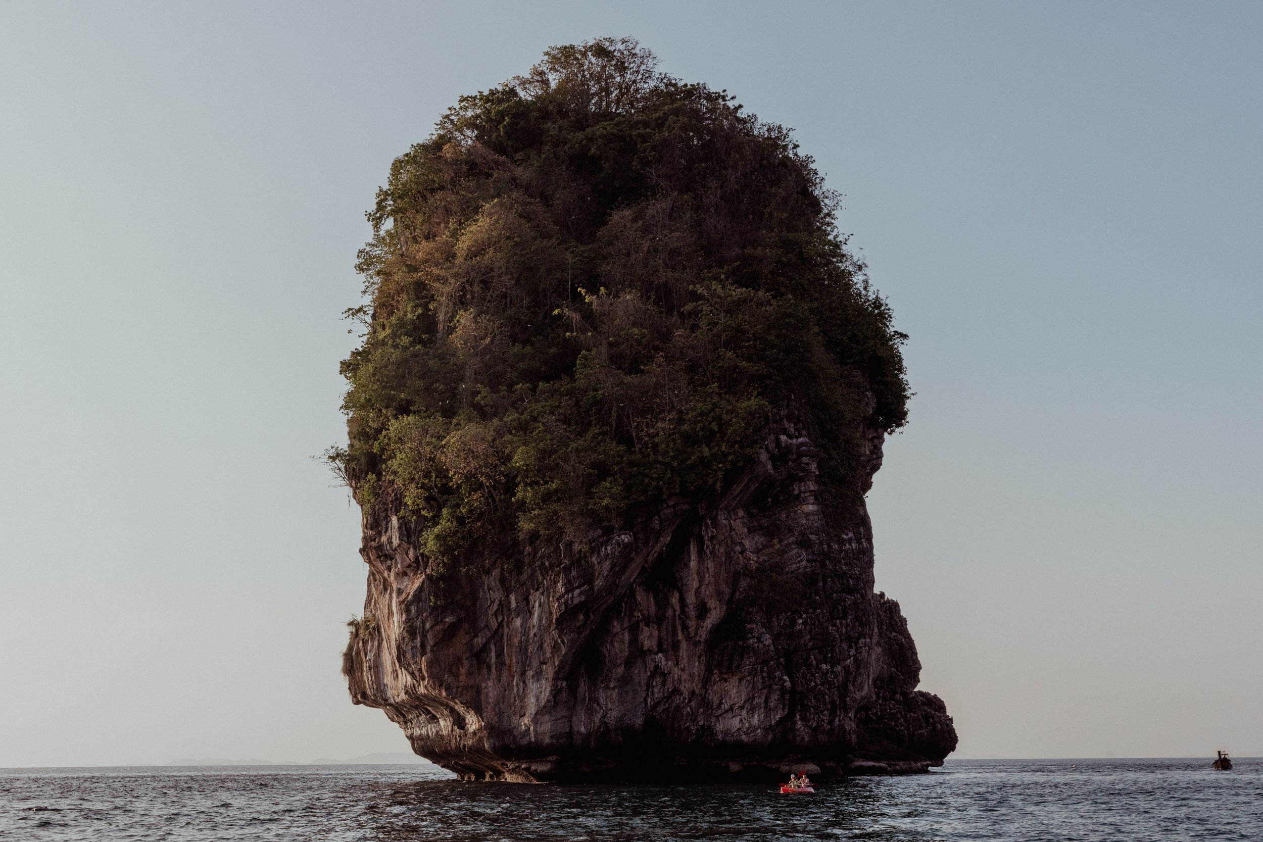 Large limestone karst formation rising dramatically from ocean waters against a clear sky.