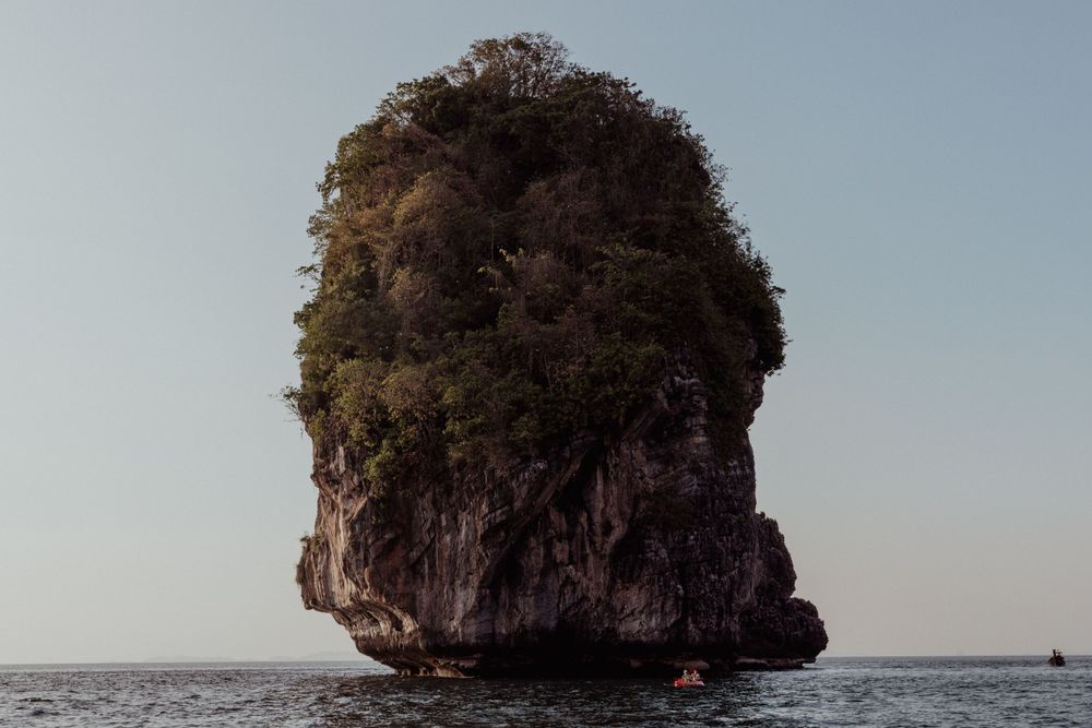Large limestone karst formation rising dramatically from ocean waters against a clear sky.