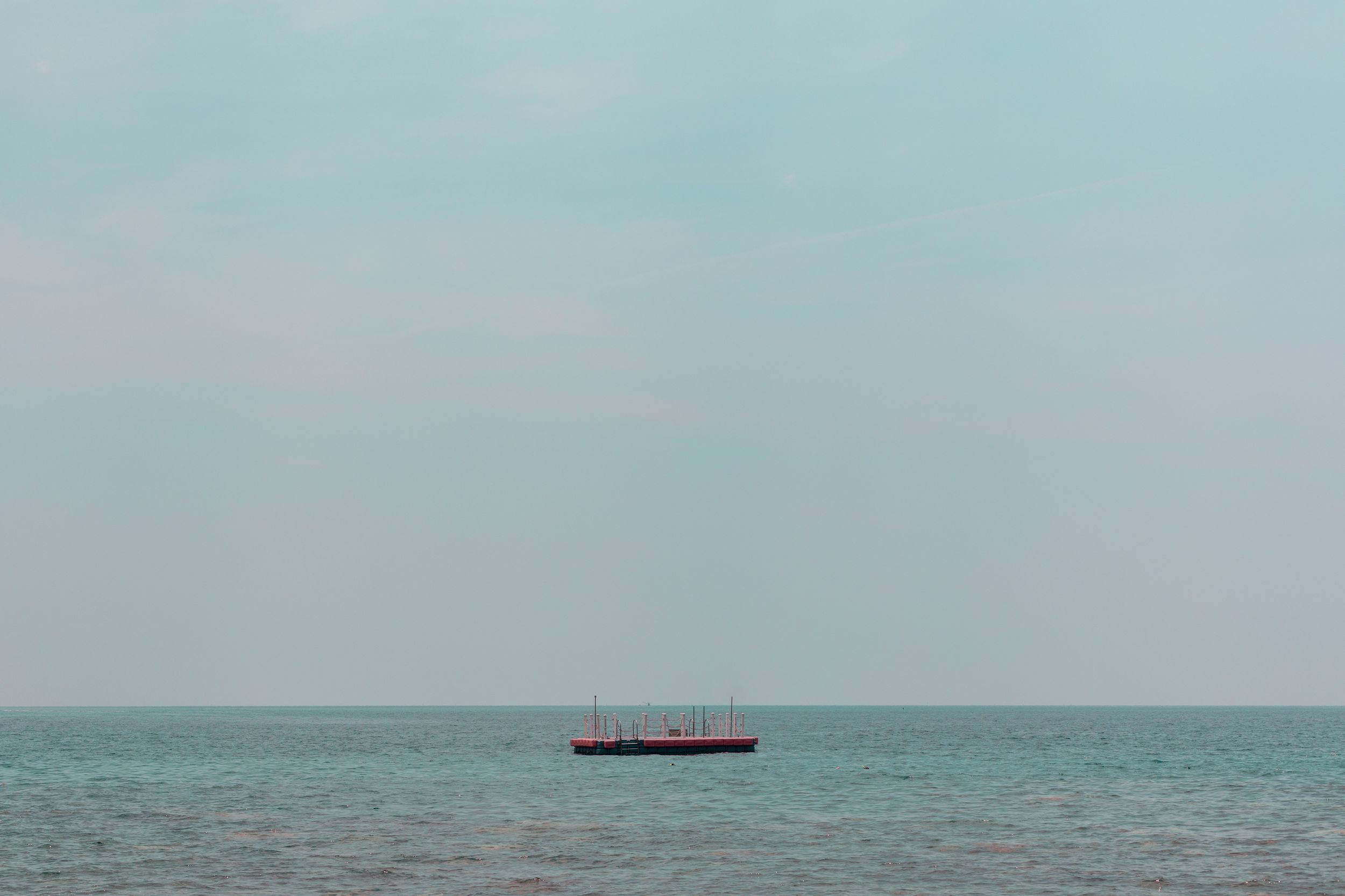 Lone cargo ship sailing on a misty turquoise ocean under pale sky.