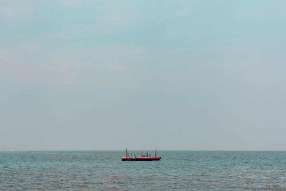 Lone cargo ship sailing on a misty turquoise ocean under pale sky.
