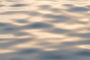Abstract pattern of sunlight reflecting on rippling water surface creating a dreamy golden texture.