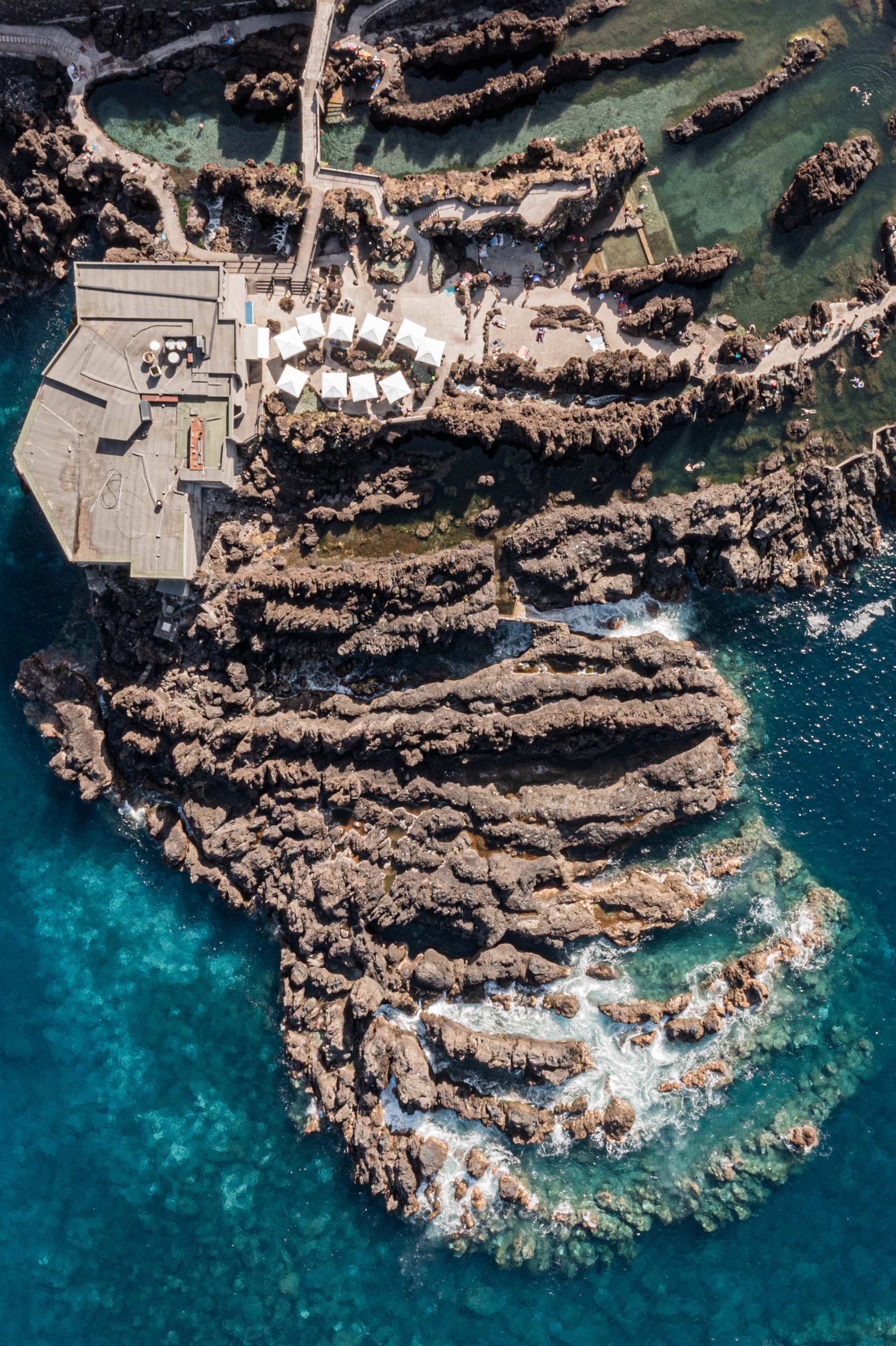 Aerial view of rocky coastline with white buildings perched on cliffs above turquoise waters.