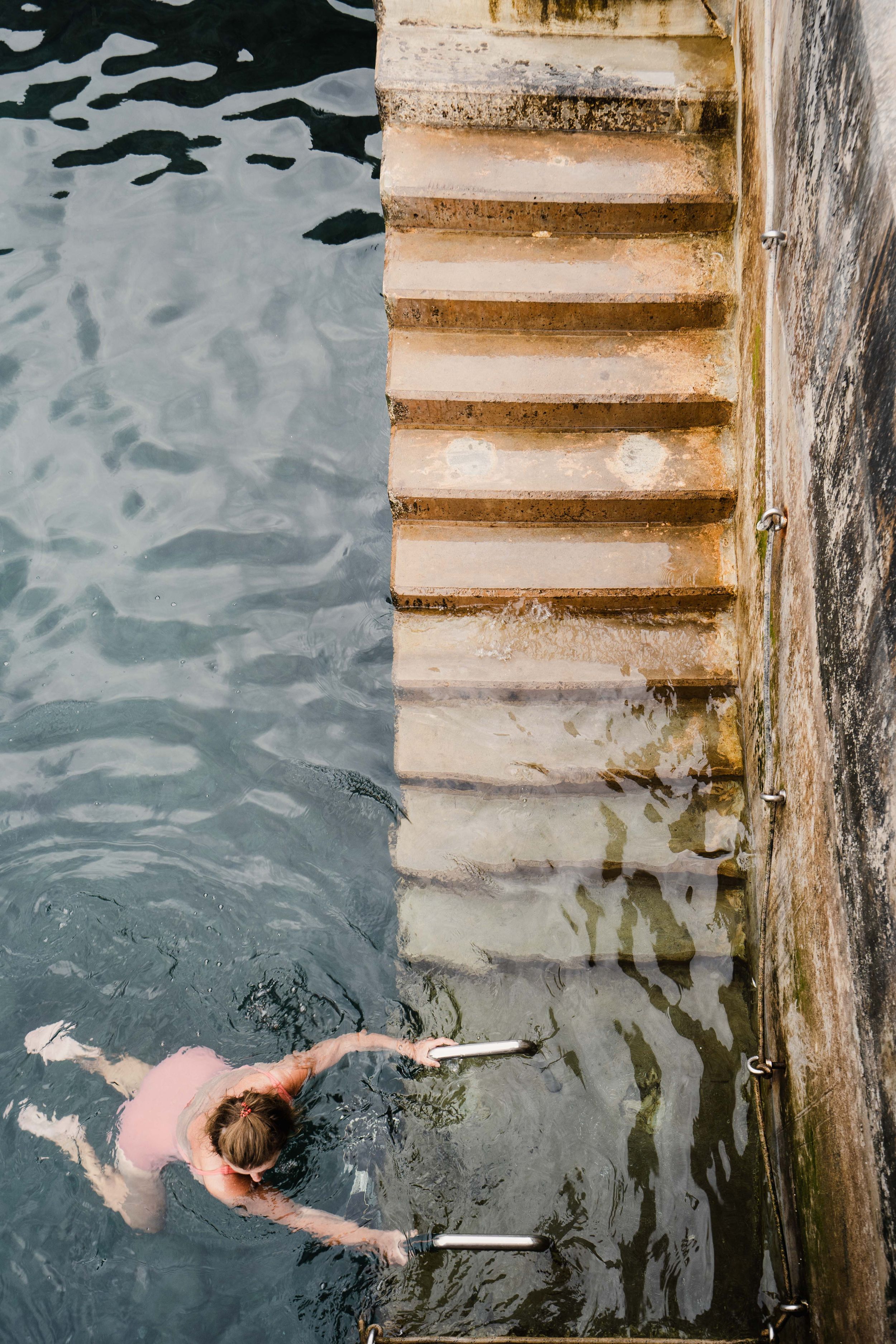 Stone steps descending into rippling water at a seaside swimming spot.